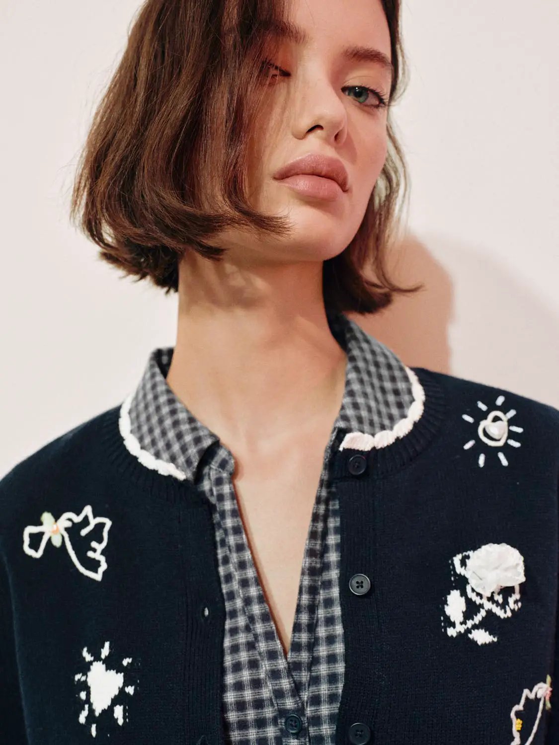 Graphic long sleeve ribbed knit cardigan in navy with white embroidery, worn over a checkered shirt
