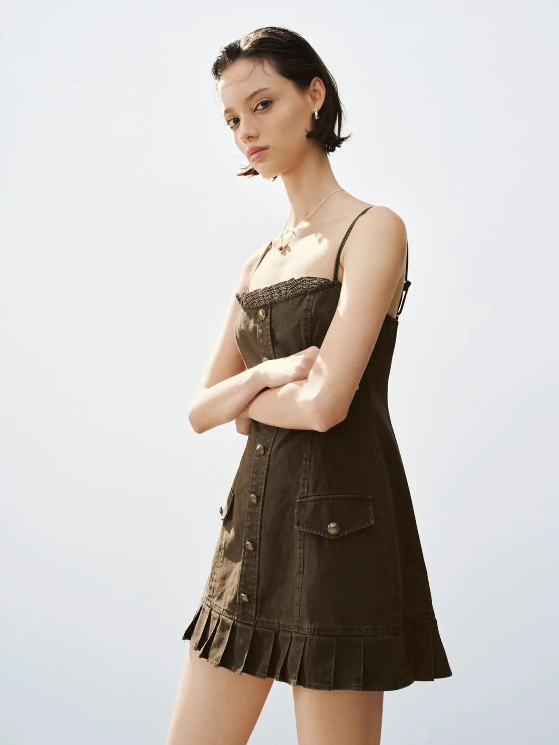 A-Line dress in dark brown denim with spaghetti straps, button-front, patch pockets, and pleated hem