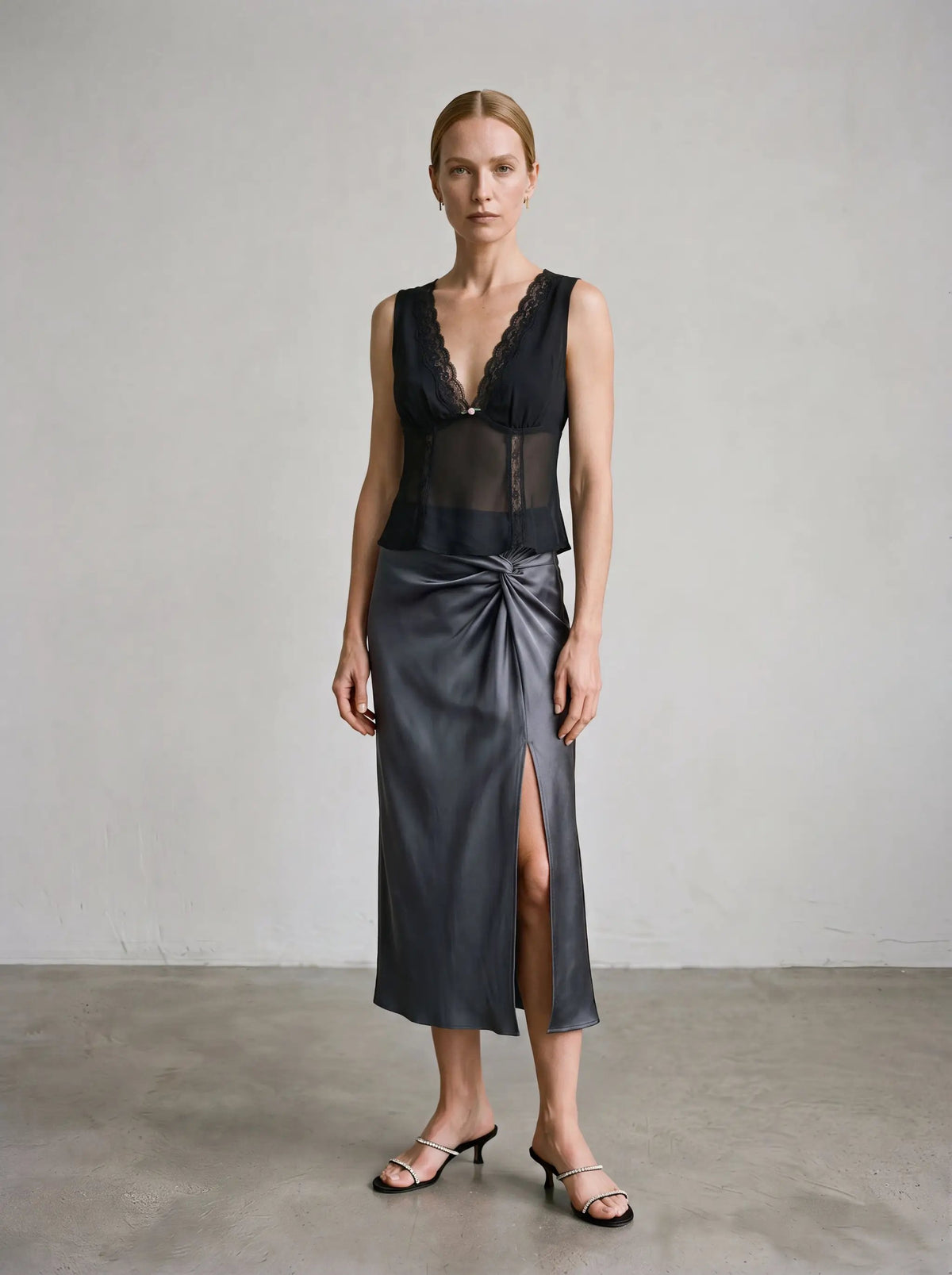 Delicate black lace-trimmed sheer V-neck blouse paired with a satin skirt on a model