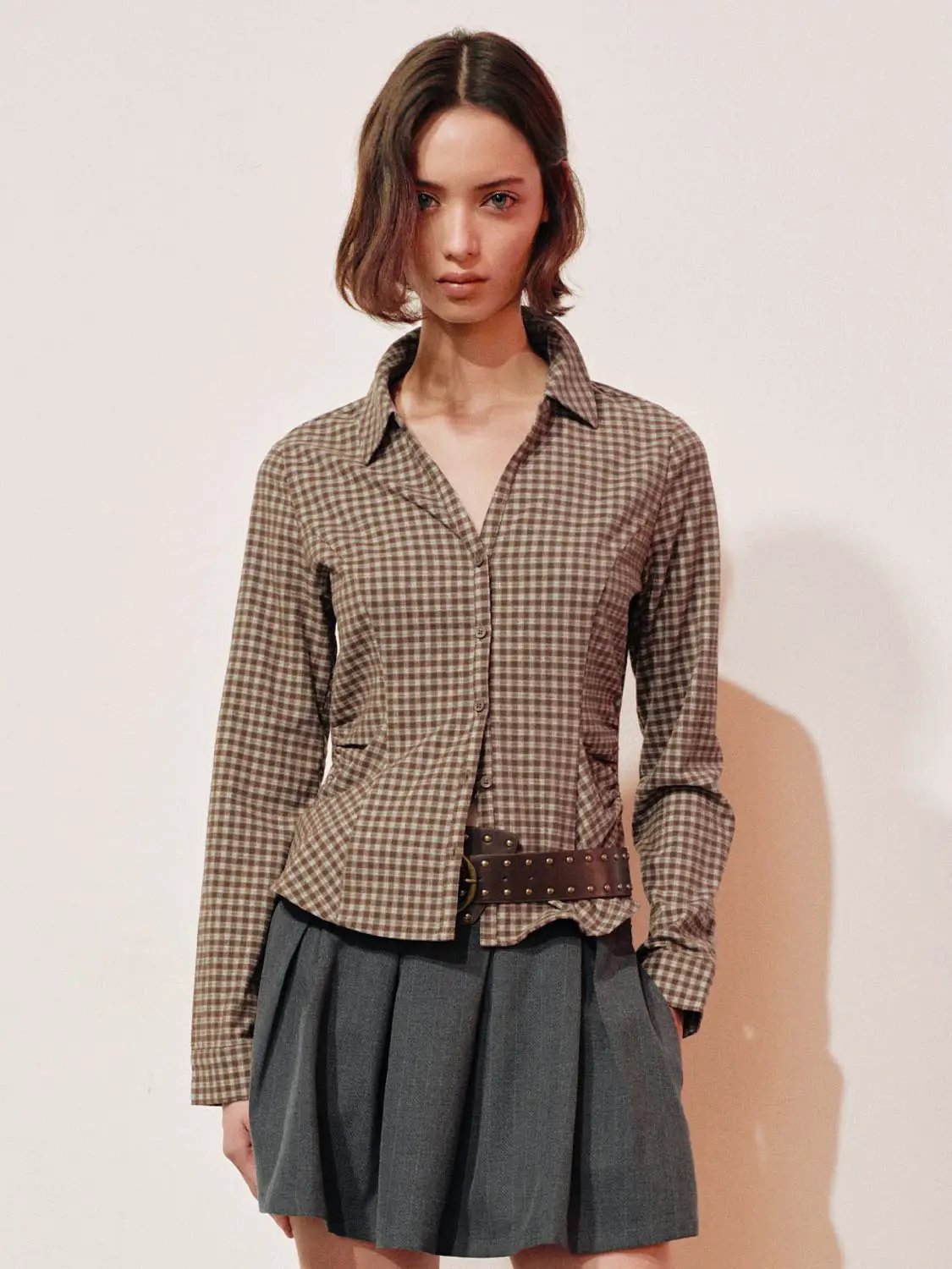 Button-front shirt in brown gingham with a collared neckline, paired with a gray pleated skirt and studded belt