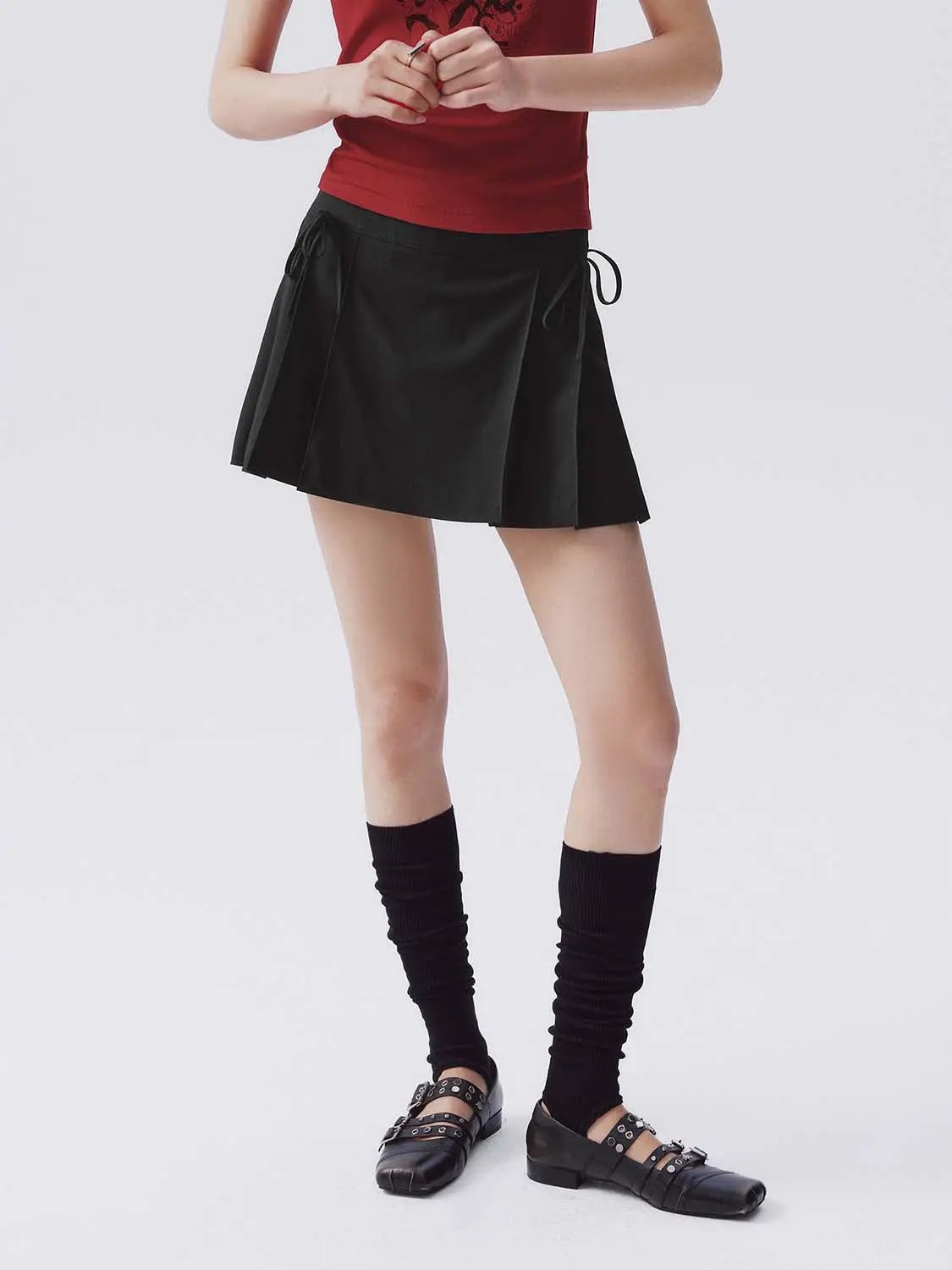 Stretch Skort, black pleated fabric with side drawstrings; worn with red top and black knee‑high socks