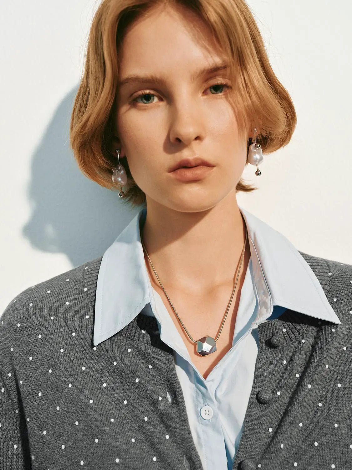 Knitted cardigan in grey with white polka dots, worn over a light blue shirt.
