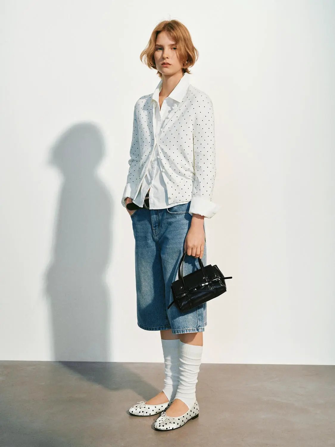 Knitted cardigan, white with black polka dots, worn over a white shirt on a model.