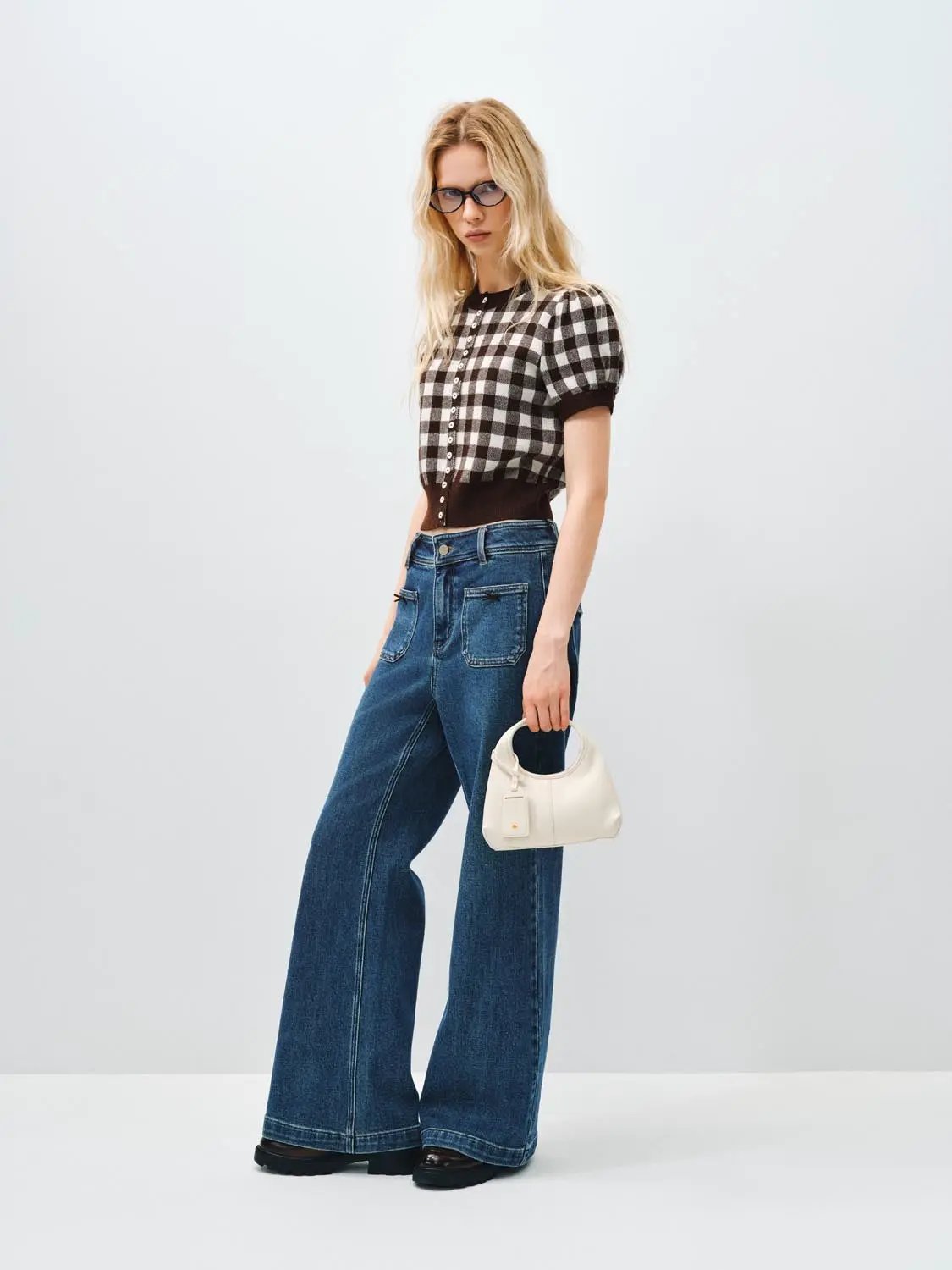 Knitted cardigan with black-and-white checks and dark rib trim, paired with wide-leg denim jeans and a white handbag.