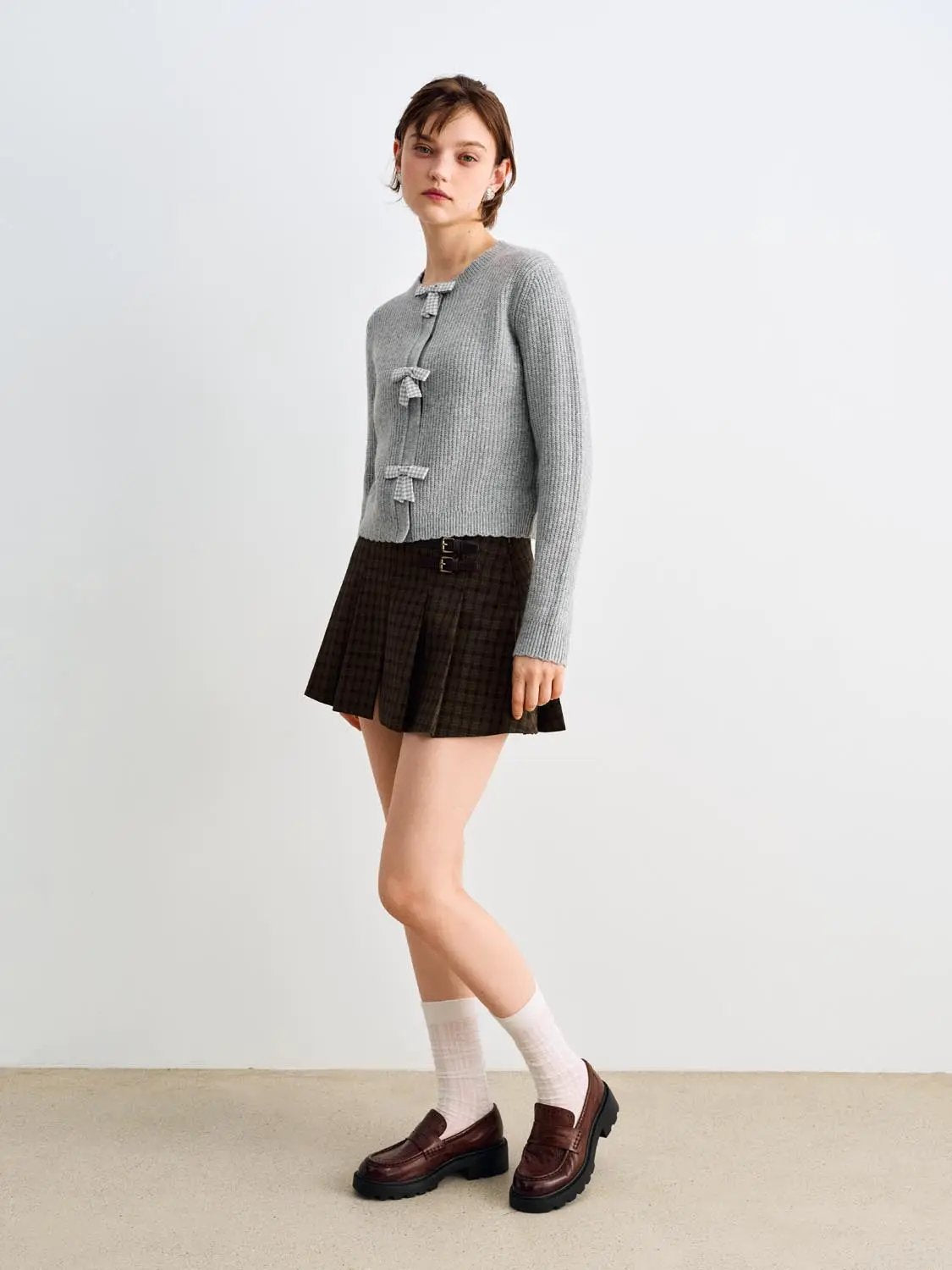 Knitted cardigan in grey with bow-front closures; styled with a brown plaid skirt.