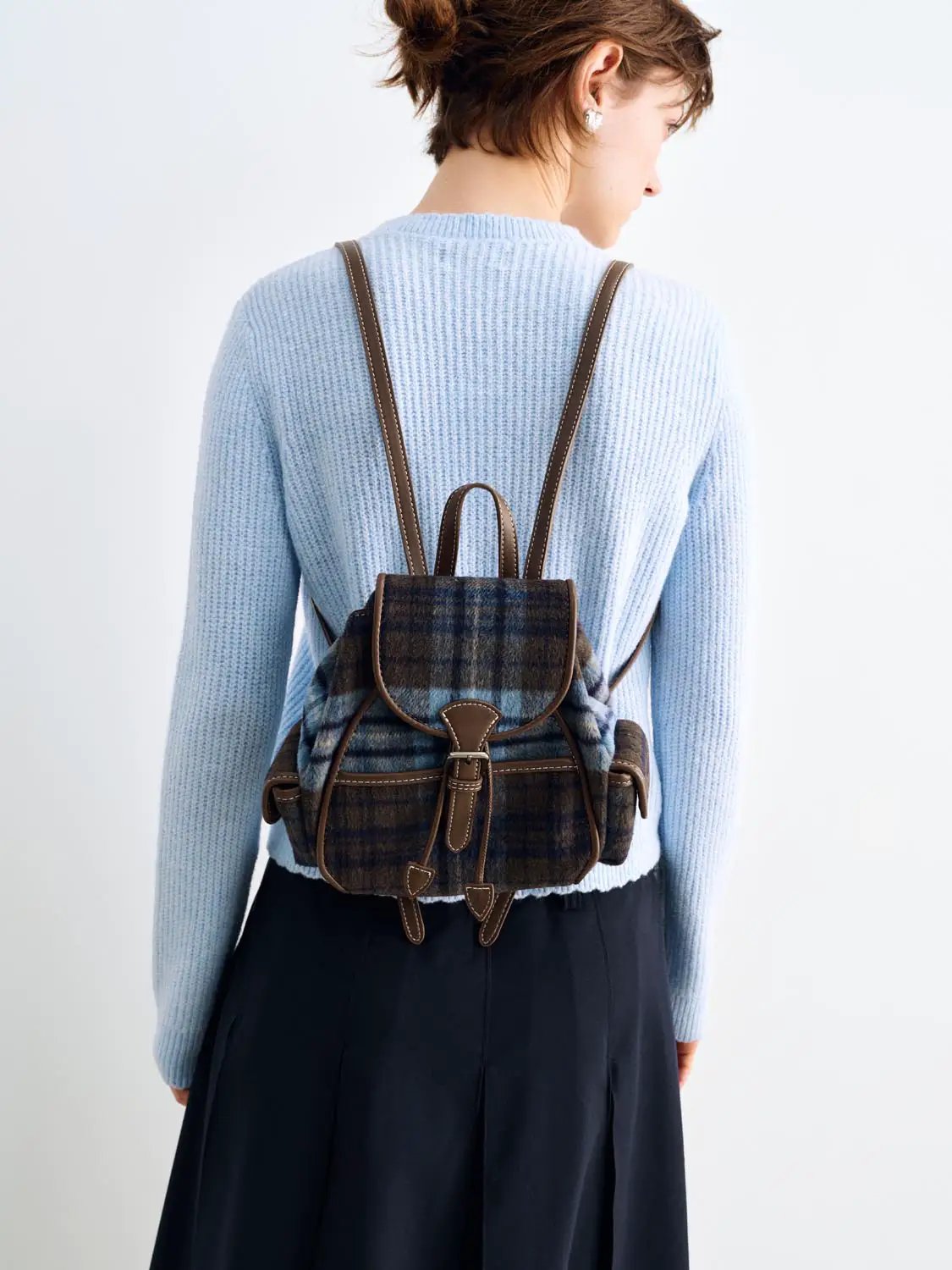 Knitted cardigan in light blue worn by model with brown leather backpack straps.