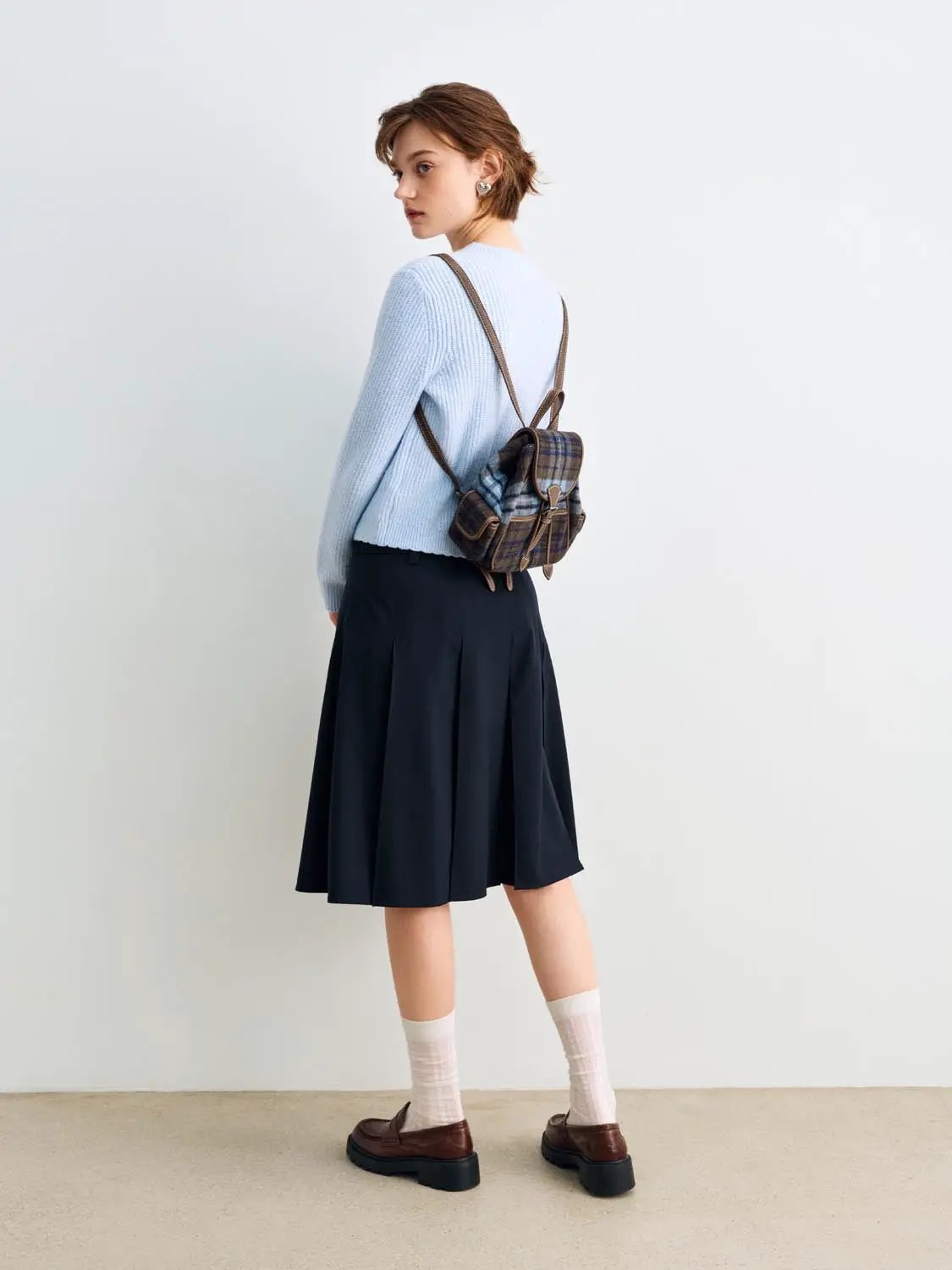 Knitted cardigan in light blue; paired with a plaid brown backpack and navy skirt