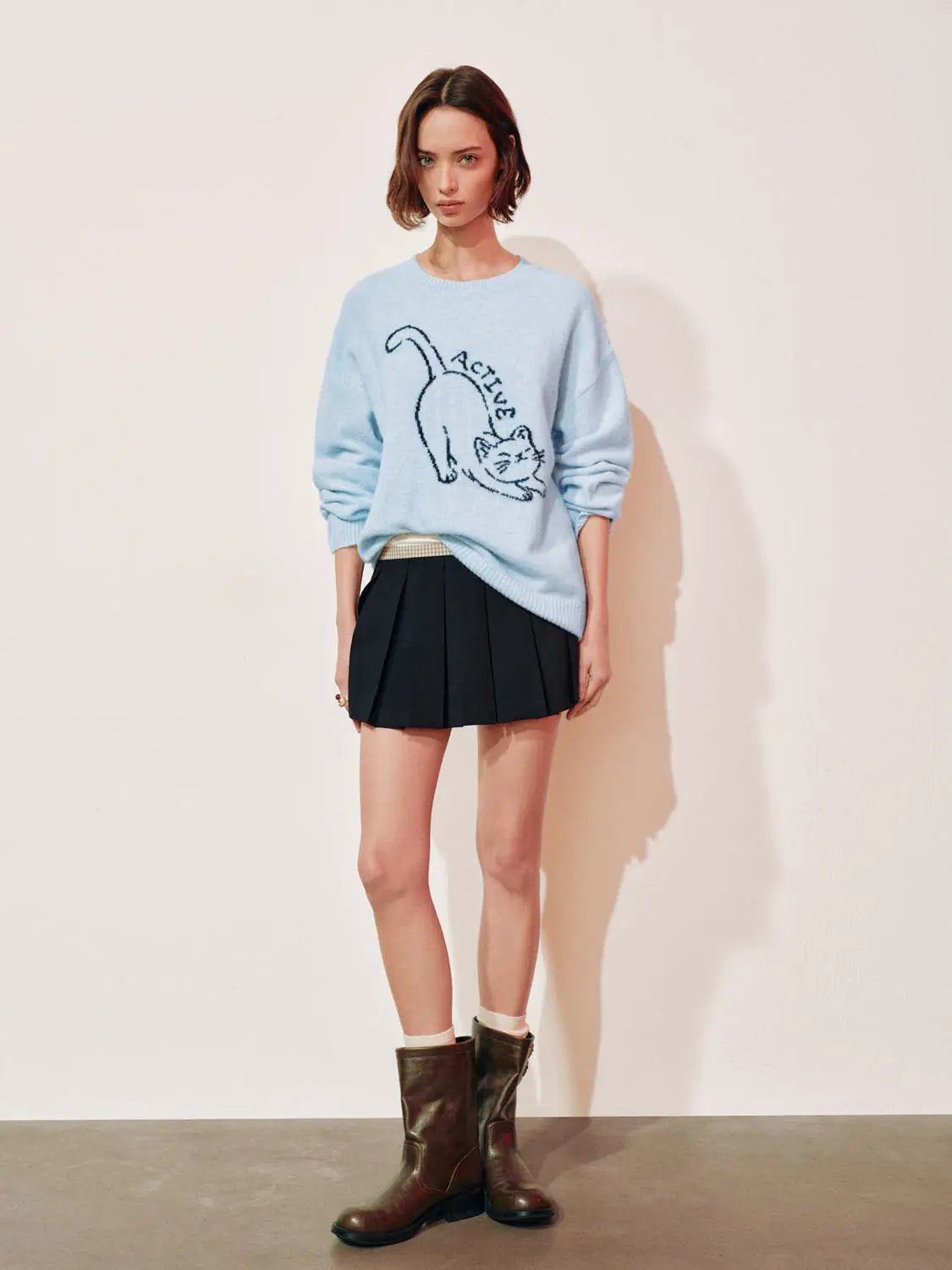 Knit T-Shirt in light blue with cat graphic, paired with black pleated mini skirt and brown boots.