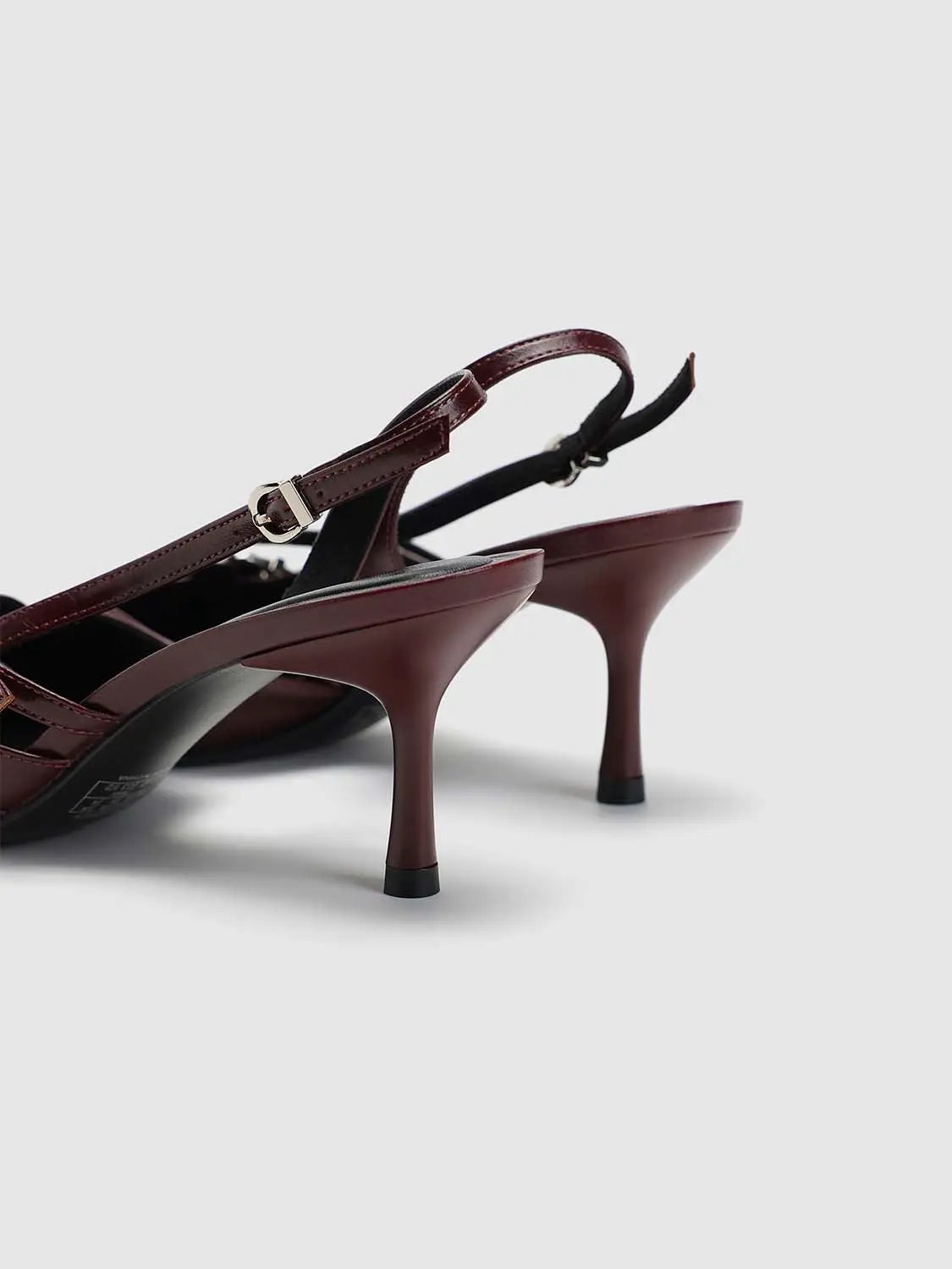 Pair of burgundy slingback heels with silver buckle and mid-height stiletto heels