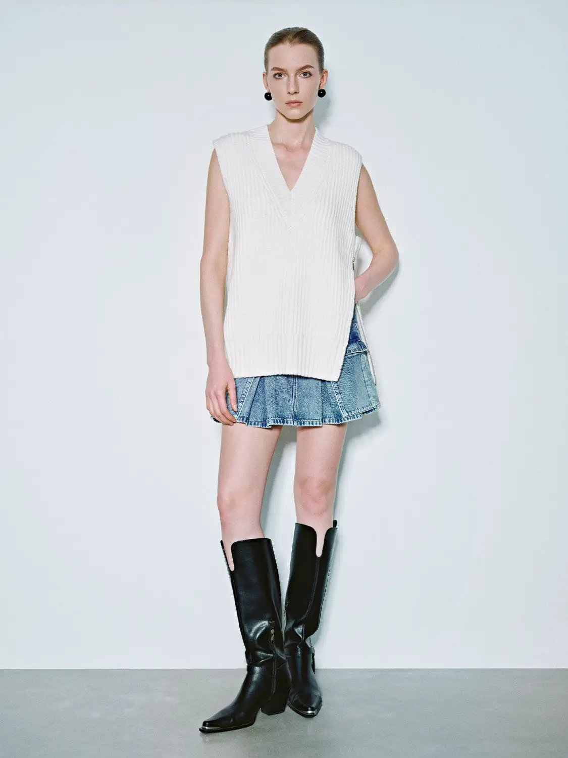 Loose V-Neck Knitted Vest, white sleeveless knit with ribbed hem, shown with denim mini skirt and black knee-high boots