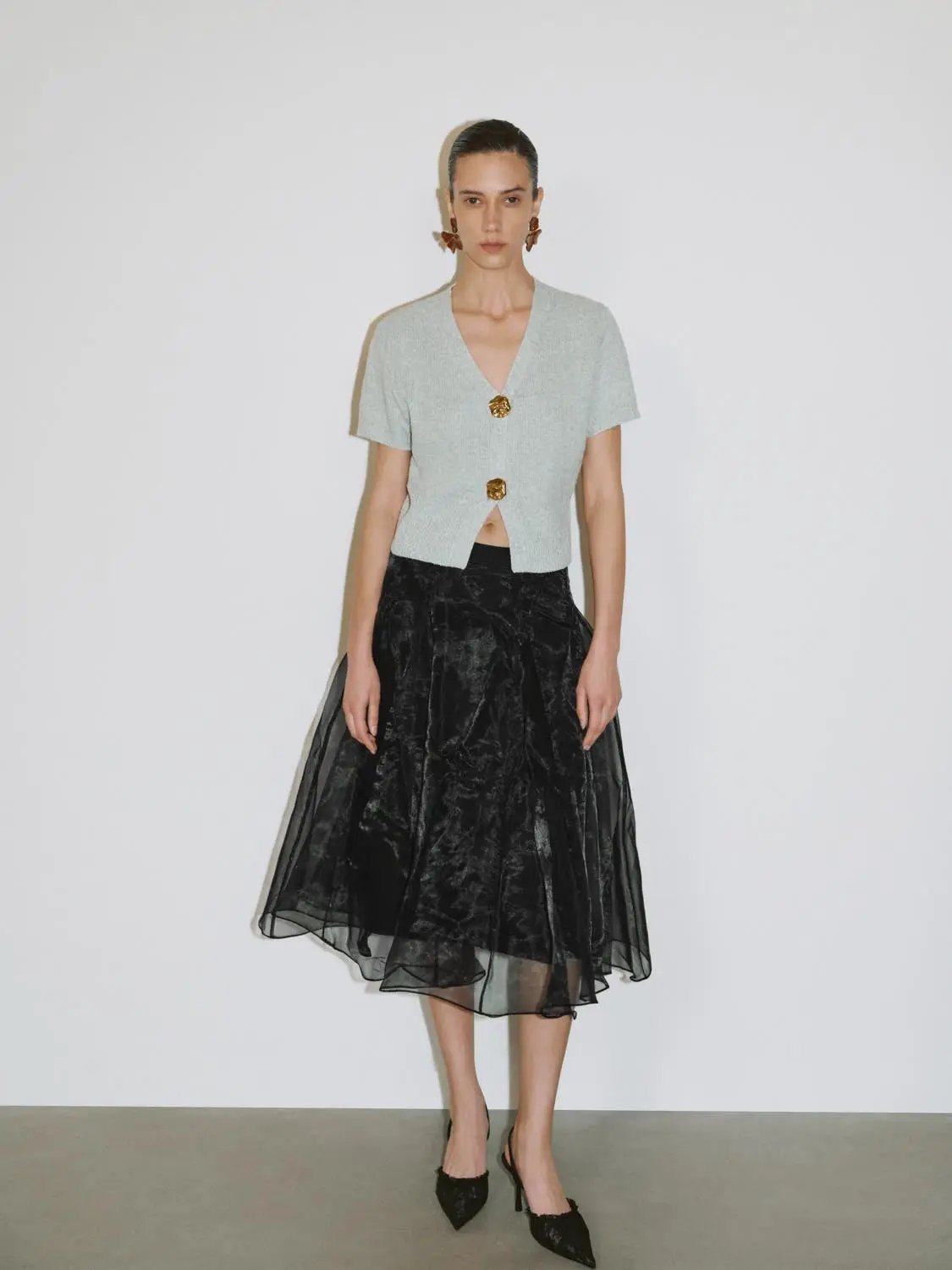 Short sleeve knitted cardigan in light gray with V-neck and two gold buttons, paired with a black tulle midi skirt.