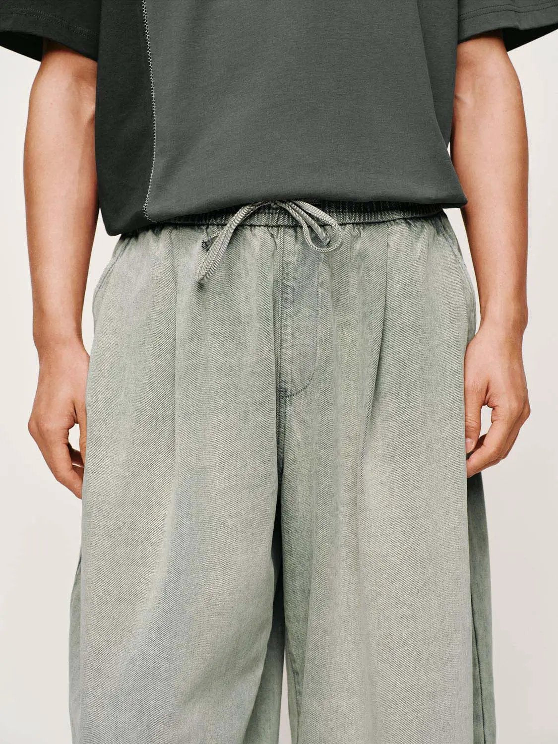 Denim jeans in light gray with drawstring waist and wide-leg fit.