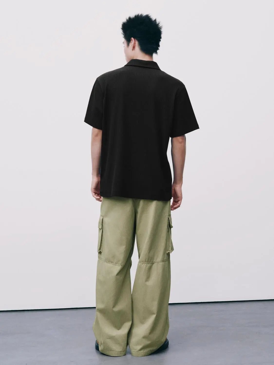 Black polo shirt on model with olive cargo pants, back view.