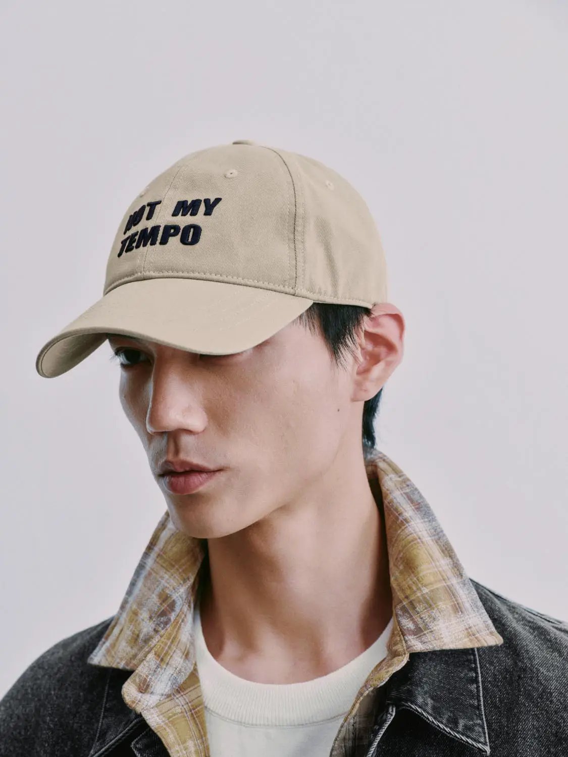 Denim jackets on a male model; dark wash denim with plaid shirt and beige cap.