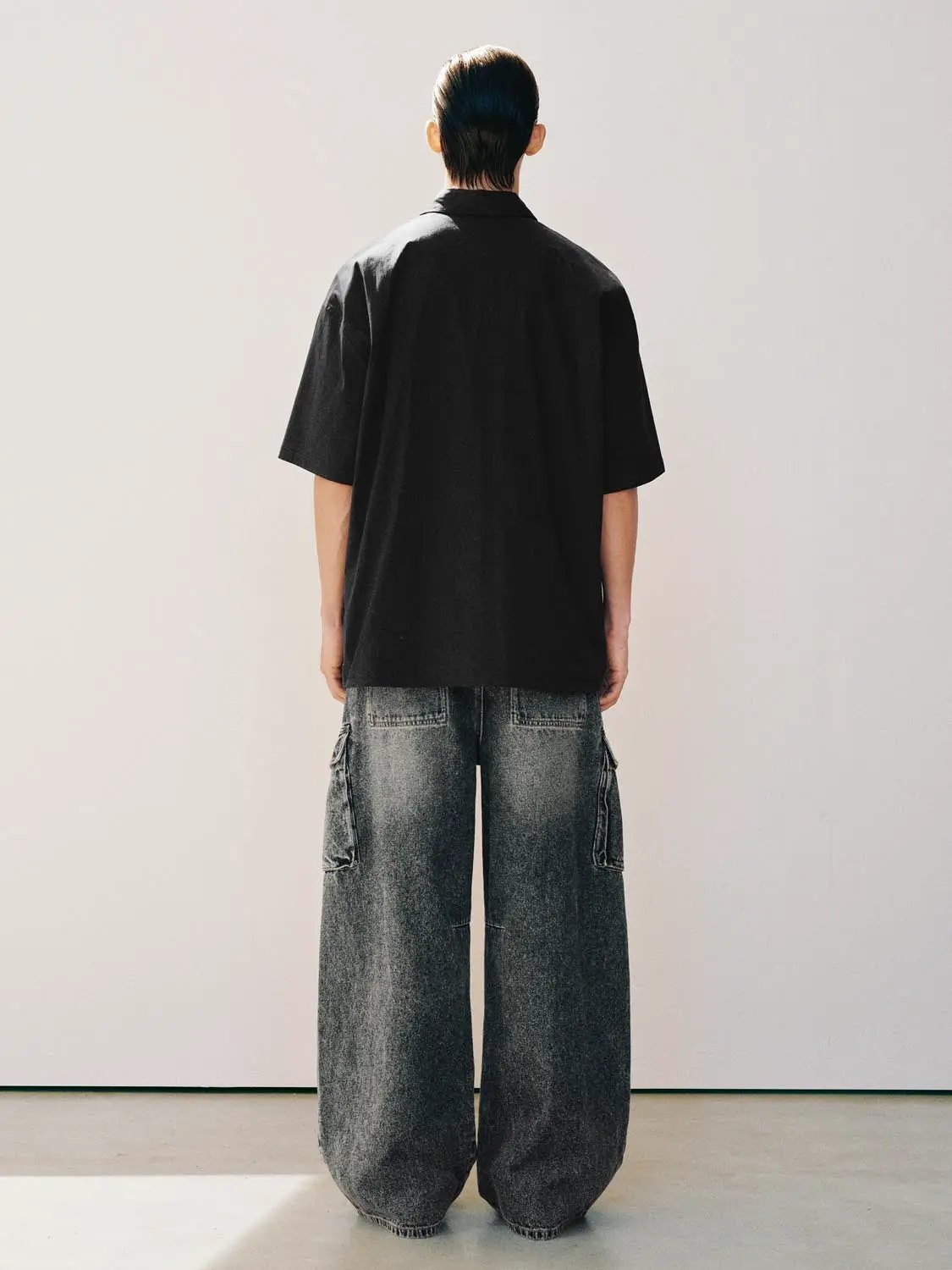 Jeans with gray washed denim, oversized wide legs and side cargo pockets; back view of model