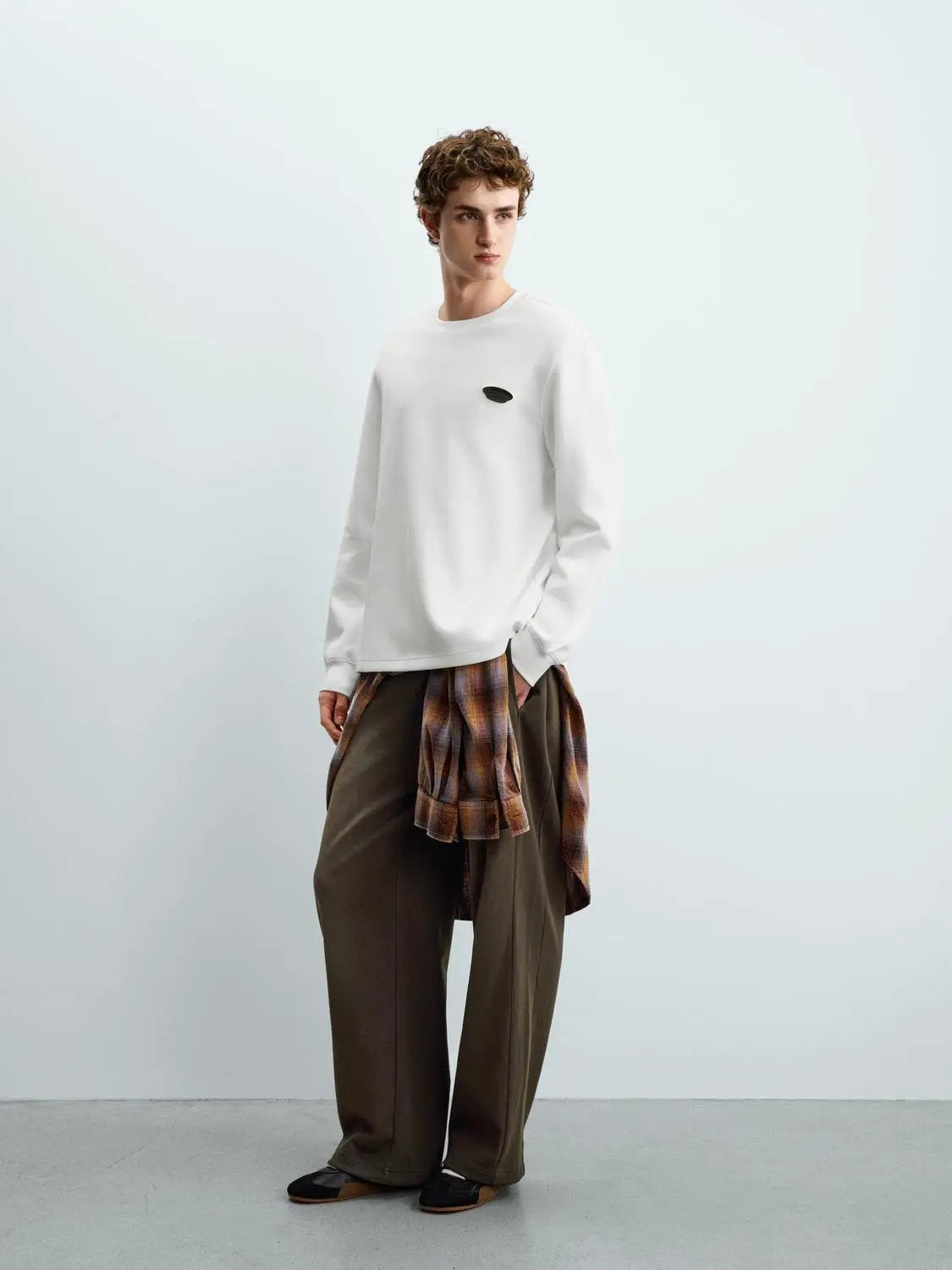 Sweatshirt by Urban Revivo, white with small black logo patch, with brown wide-leg pants and plaid shirt tied at waist.