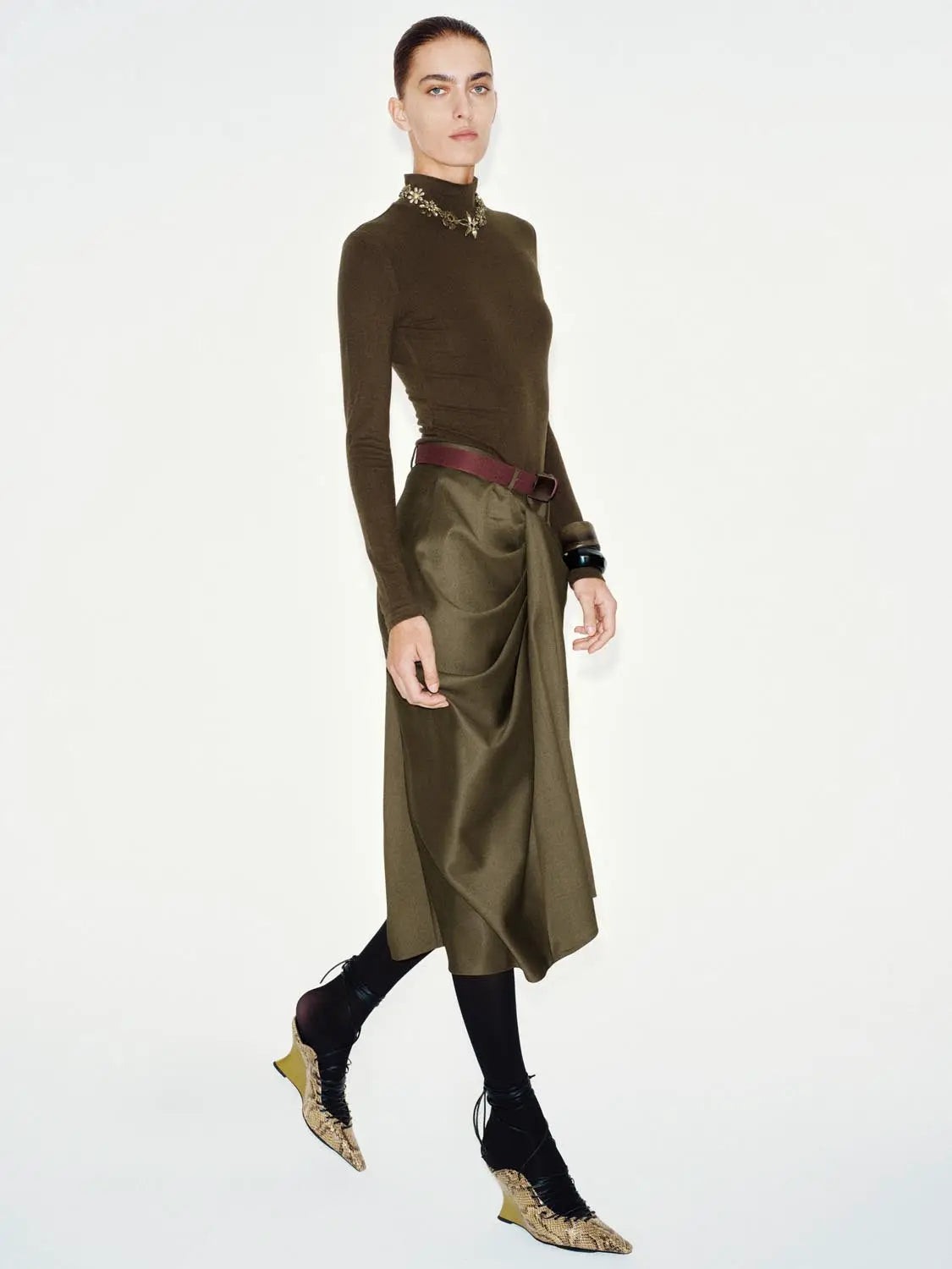 Olive-brown knit long-sleeve T-Shirt on model, paired with burgundy belt and draped olive skirt