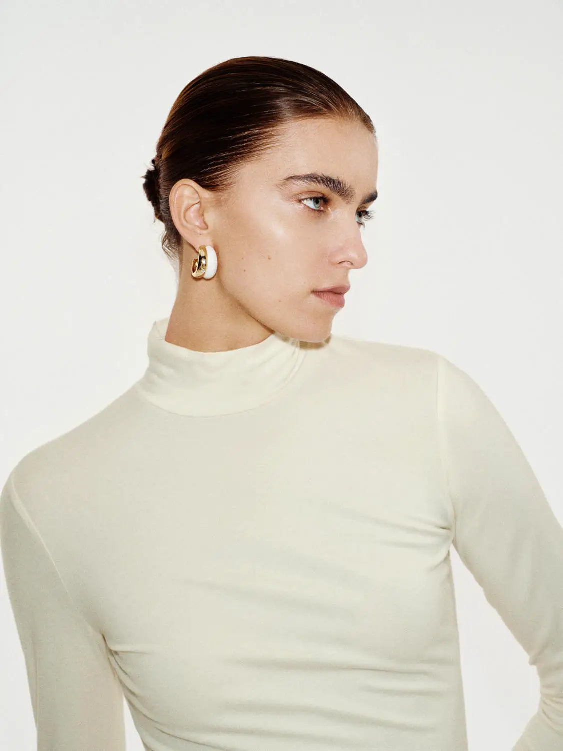 Ivory long-sleeve turtleneck T-shirt worn by model with cream and gold hoop earrings