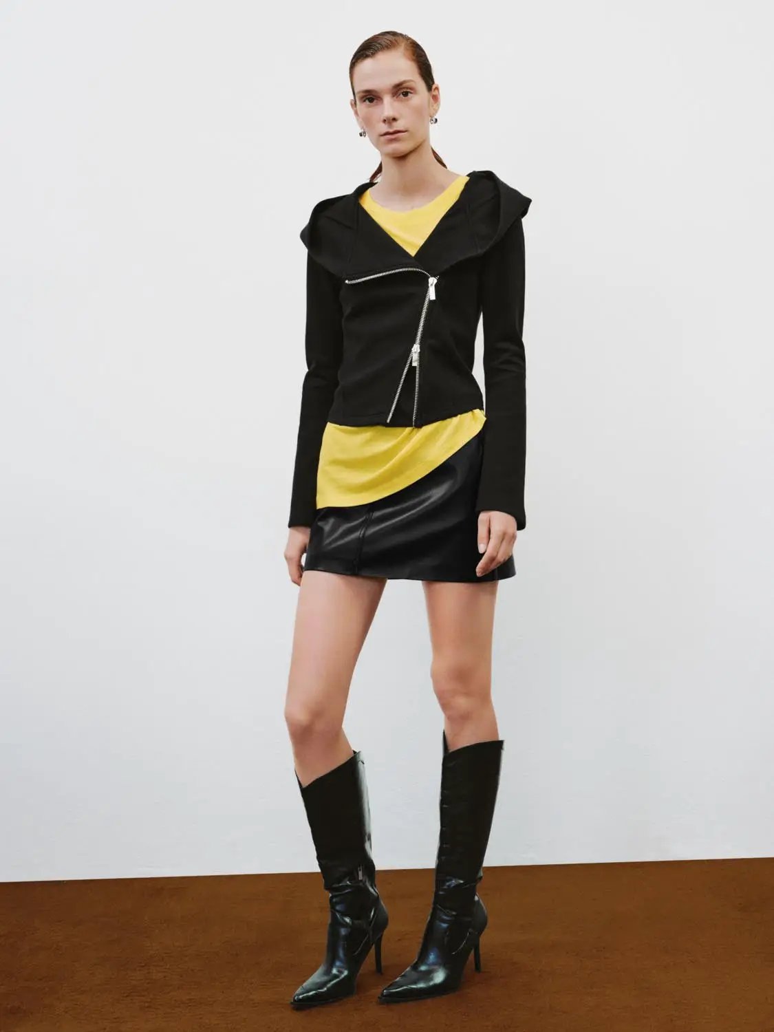 Asymmetrical-zip hooded black cotton-blend hoodie on model with yellow top peeking underneath.