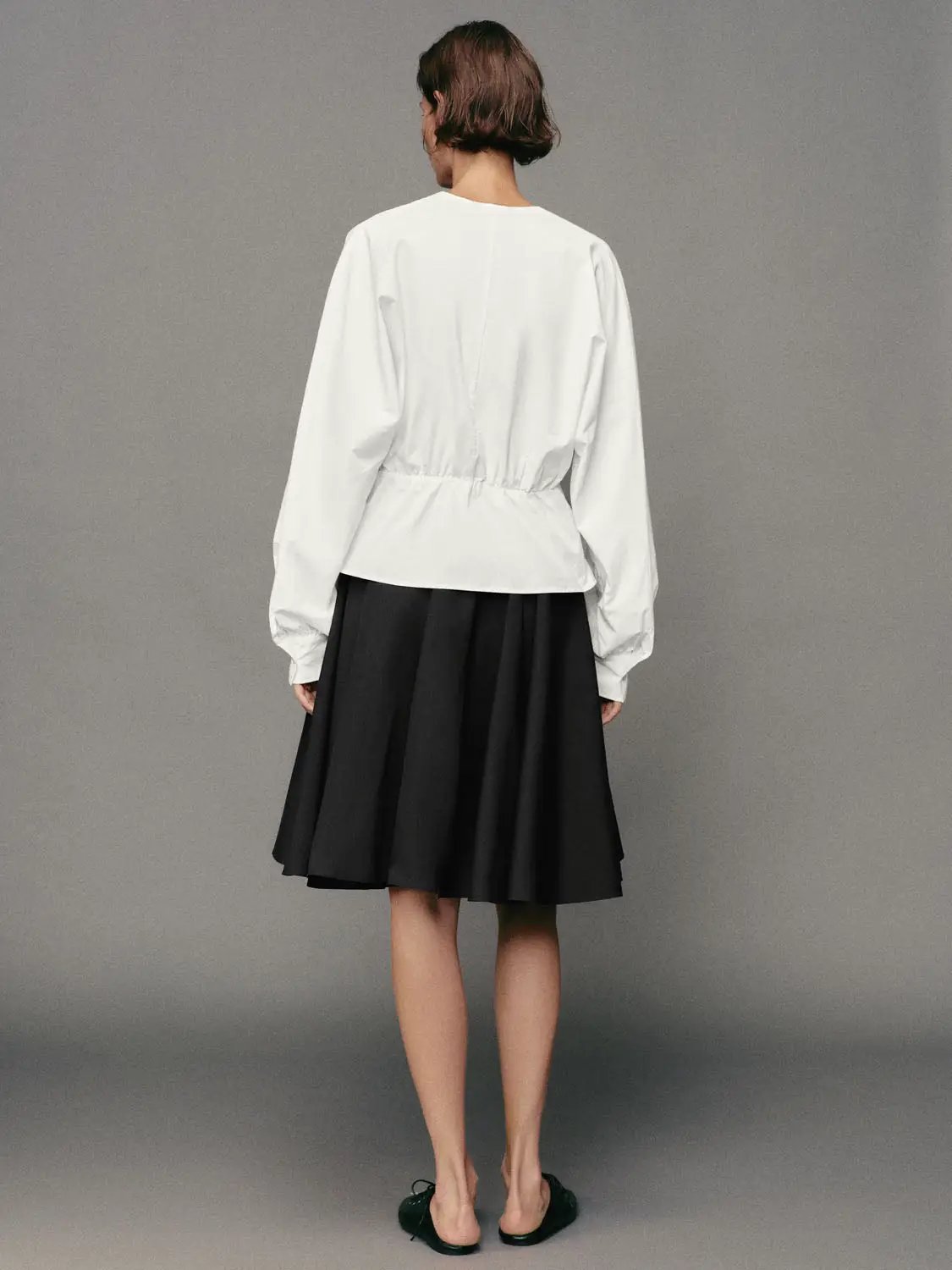 Pleated high-waisted cotton A-line knee-length skirt in black, shown on a model.