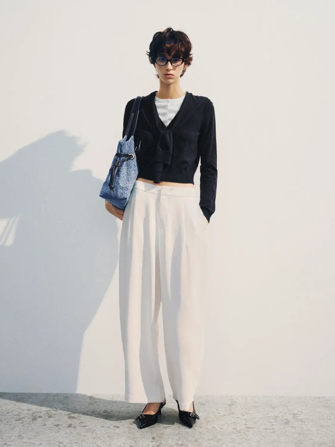 Knit T-Shirt, black cropped knit with front tie; paired with white wide-leg trousers and blue handbag.