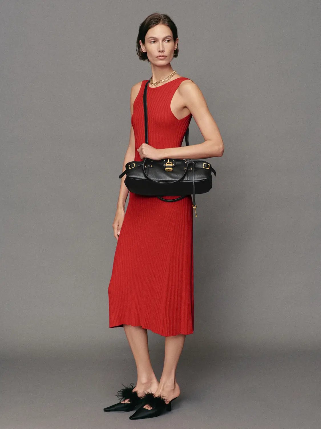 Fitted red ribbed sleeveless round-neck maxi knit dress worn with a black crossbody bag and feather-embellished black flats.