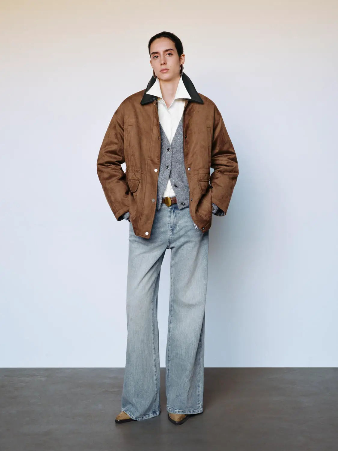 Padded jacket in brown with a dark collar, worn over white shirt and grey cardigan, with light-wash jeans.