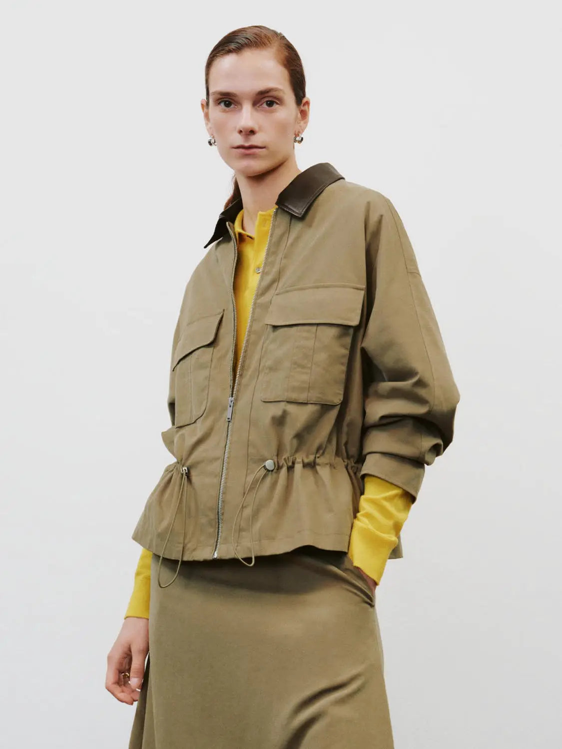 Padded jacket in olive khaki with black collar, front zip, drawstring waist, and large flap pockets.