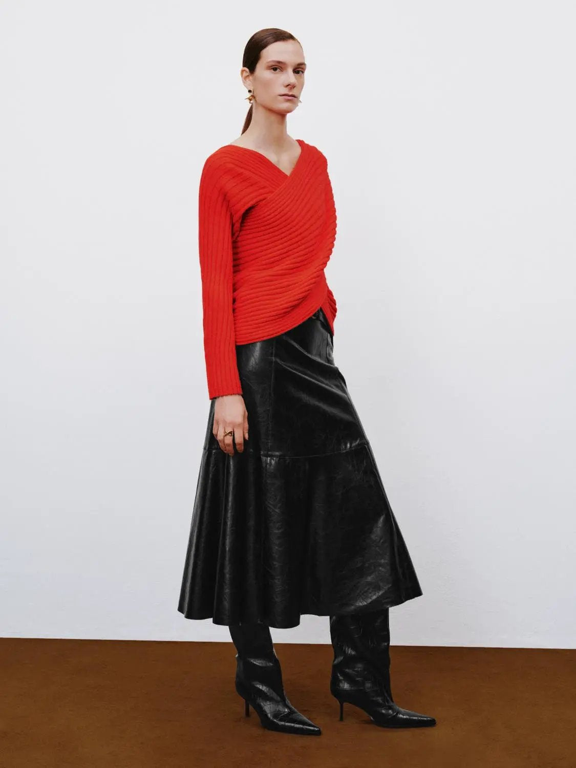 A-line skirt in black faux leather; midi-length with subtle panel seams, styled with a red ribbed knit top.