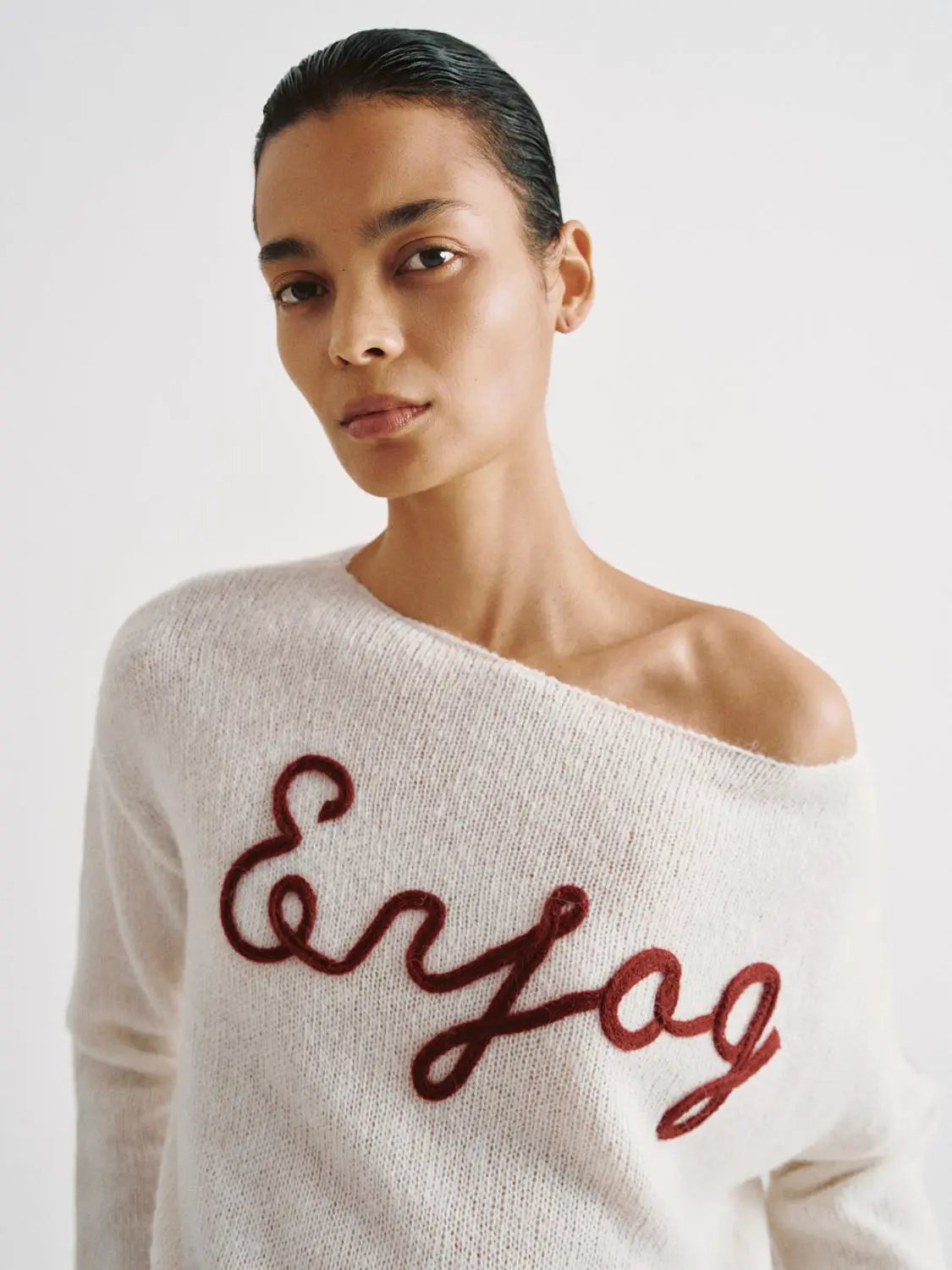 Knit lightweight sweater with red script embroidery on white fabric, off-shoulder neckline.