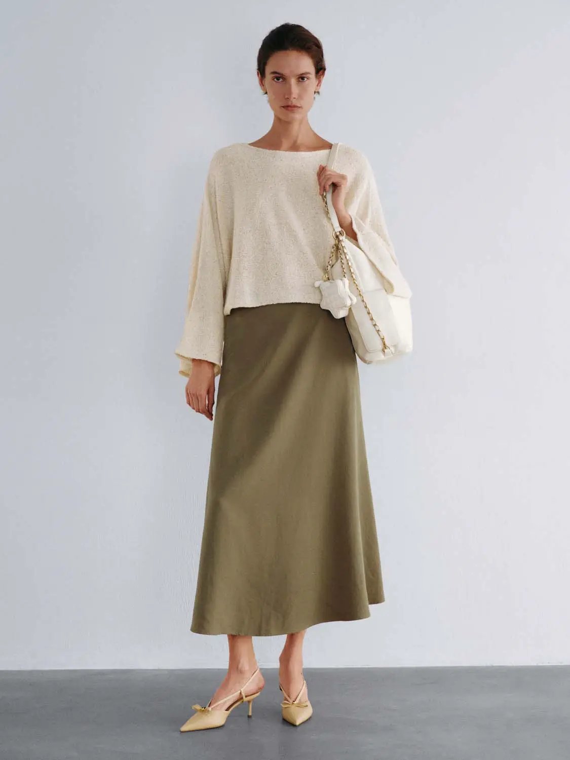 Oversized cropped textured boat-neck drop-shoulder cream knit sweater worn with olive skirt and white handbag