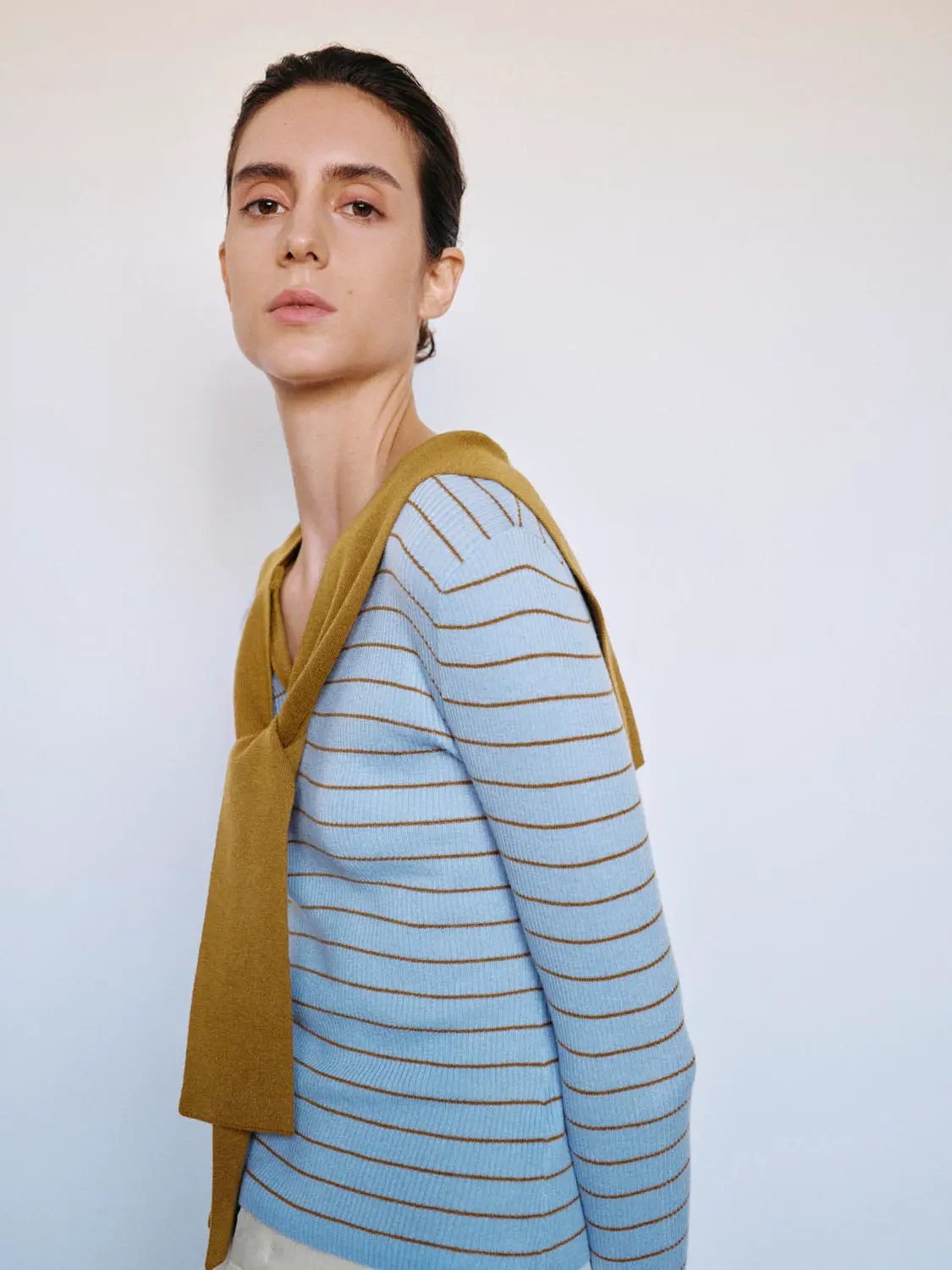 Striped light blue knit T-shirt with V-neck and long sleeves; mustard shawl draped over shoulders.