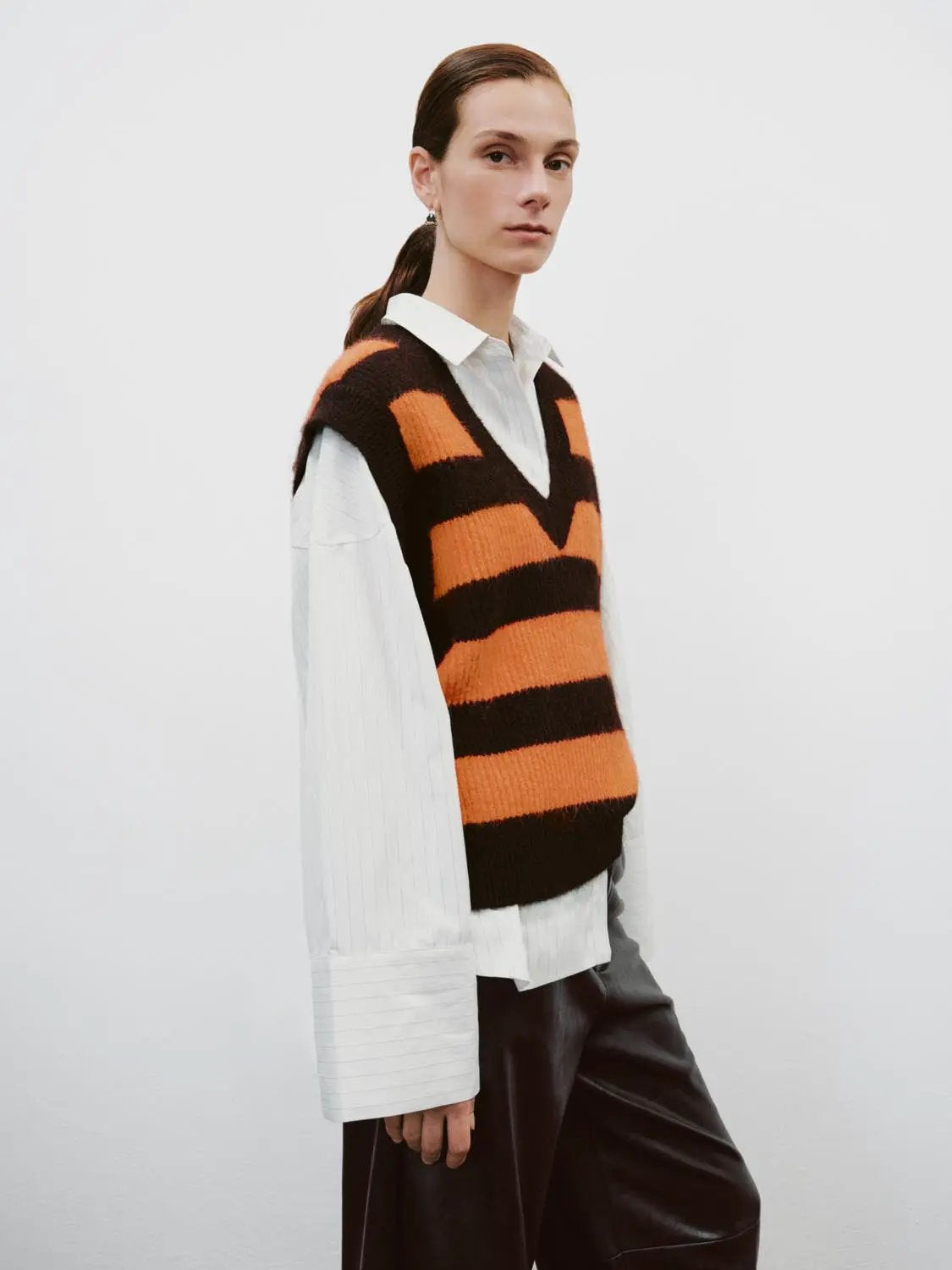 Striped stretch knit V-neck sleeveless tank top in orange and black, worn over a white shirt.