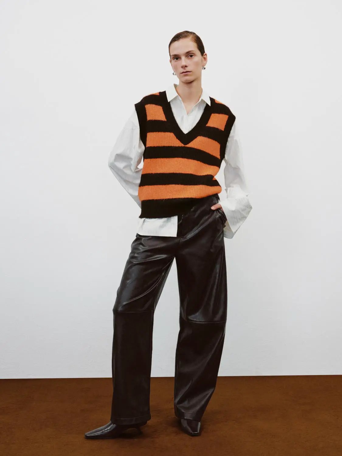 Striped orange-black knit V-neck sleeveless tank top with bold horizontal bands styled over a crisp white shirt