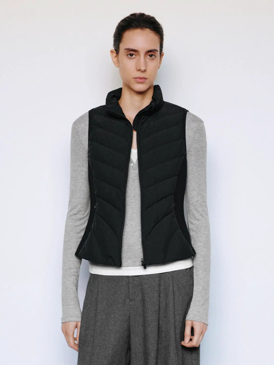Down vest from Urban Revivo Fashion in black quilted fabric with stand collar worn over a grey long-sleeve top