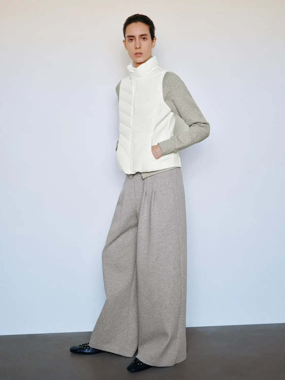 White down puffer vest worn over gray knit sleeves, paired with wide-leg gray trousers
