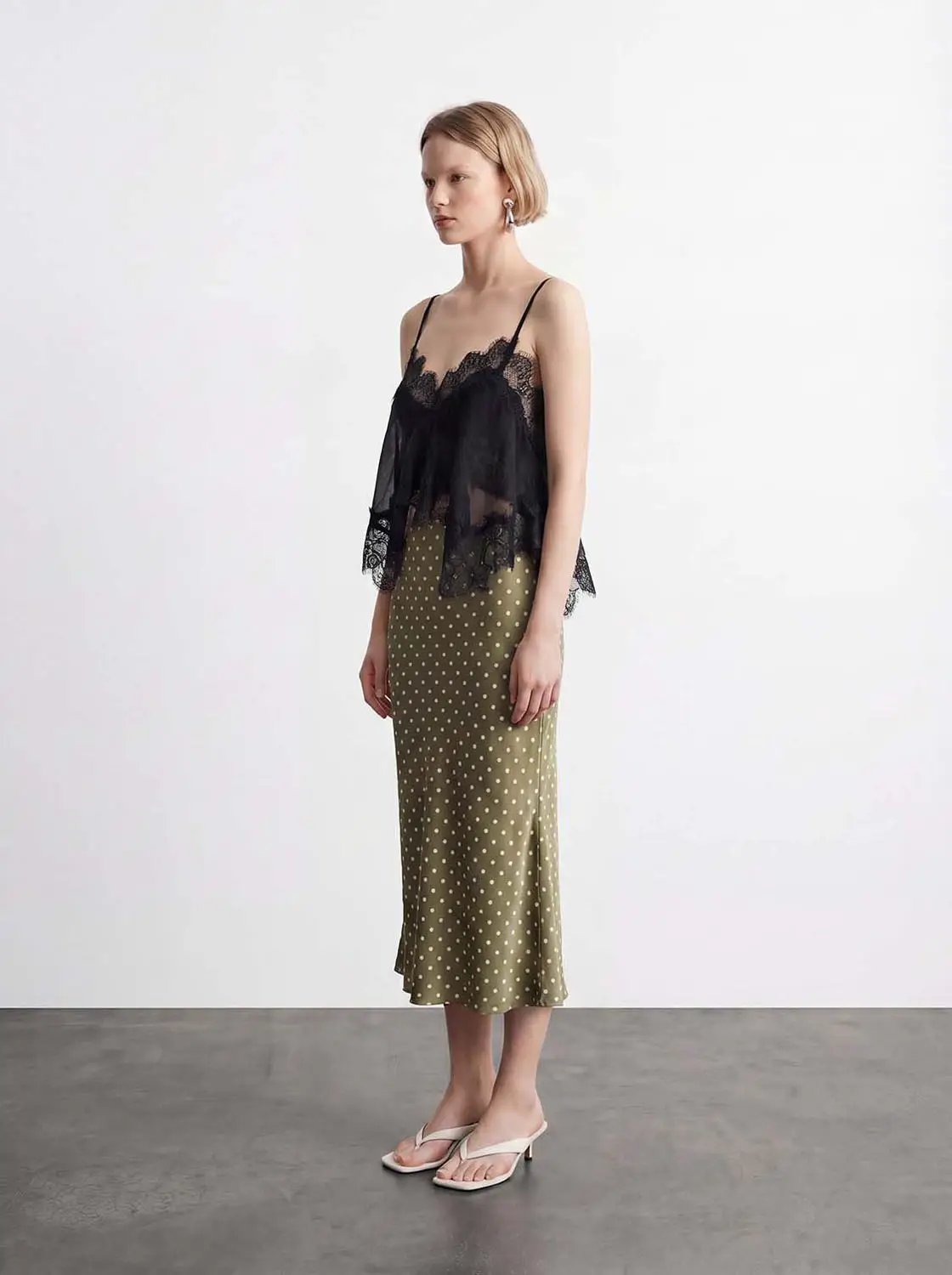 Camisole top, black lace with sheer overlay and thin straps; paired with an olive polka-dot midi skirt.