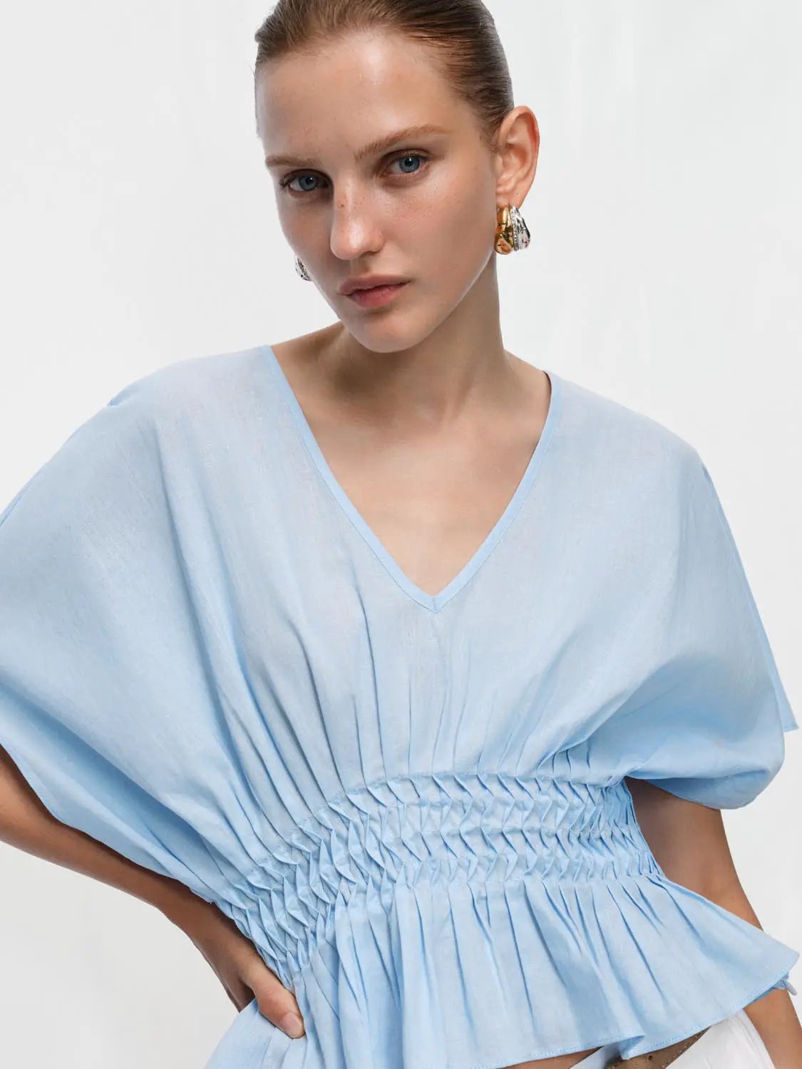 Blue V-neck puff-sleeve blouse with a smocked waist in a cotton-linen blend.