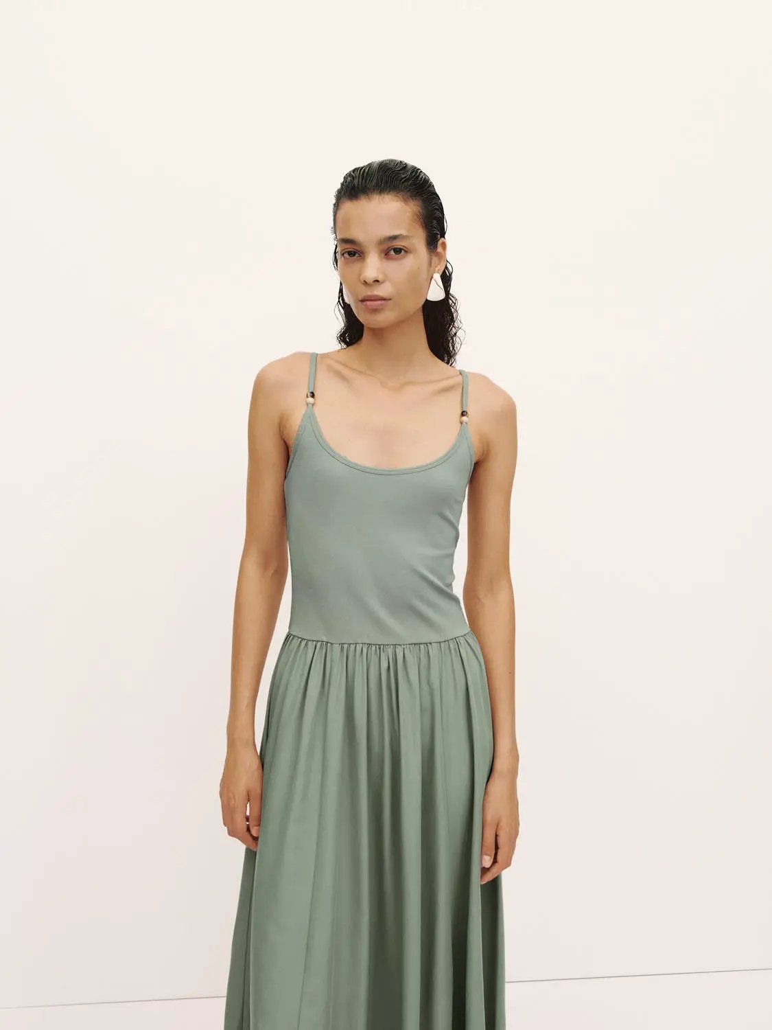 A-line dress in sage green with thin shoulder straps and a flowing maxi skirt