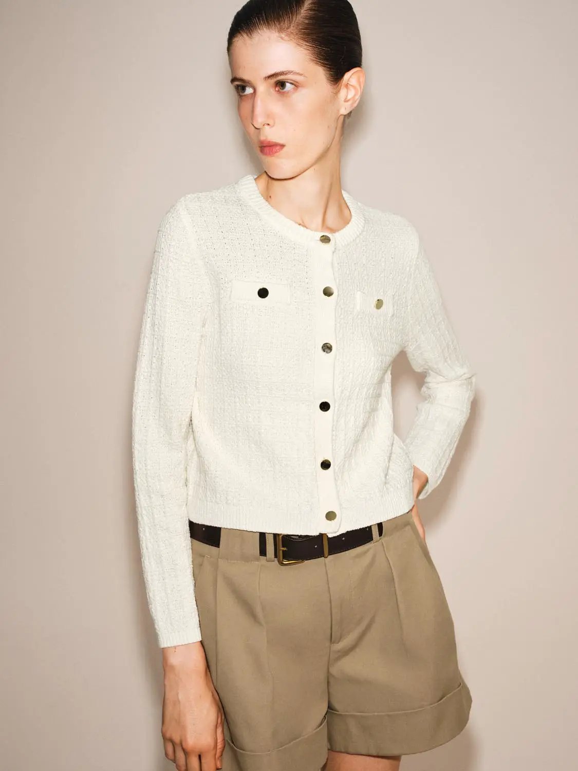 Knit cardigan, white textured knit with gold buttons and front chest pockets, paired with khaki shorts.