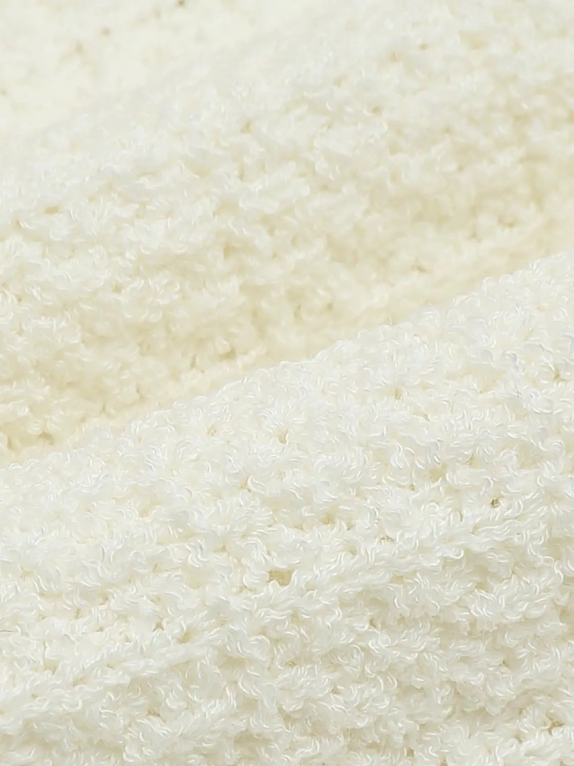 Knitted cardigan fabric in cream with boucle texture close-up.
