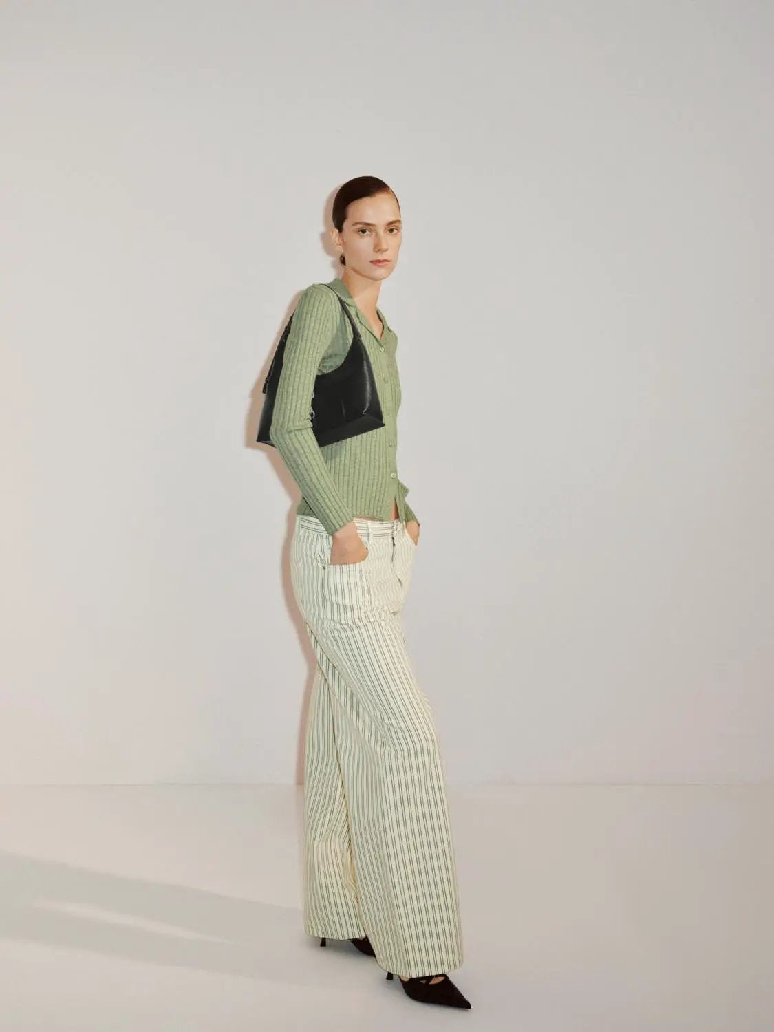 Ribbed cotton-blend shirt-collar cardigan in pale green worn by a model, with striped wide-leg pants and a black handbag.
