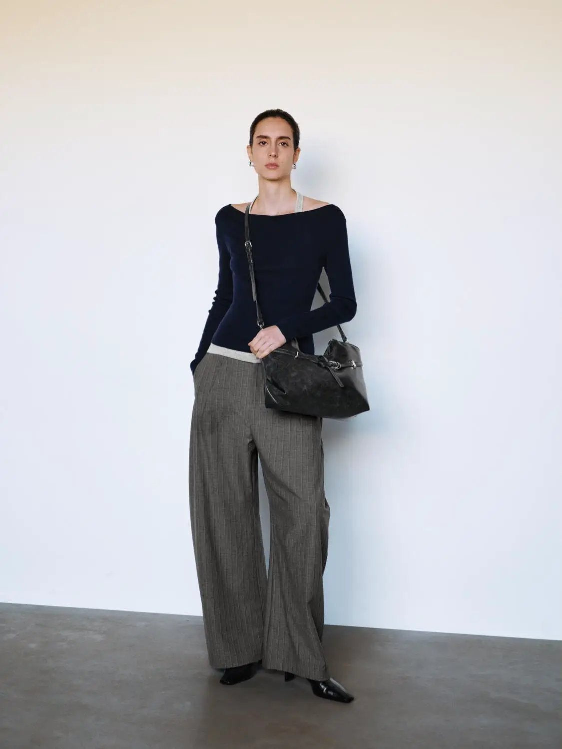 Fitted navy boat-neck long-sleeve knit top worn with gray pinstripe wide-leg trousers and a crossbody bag
