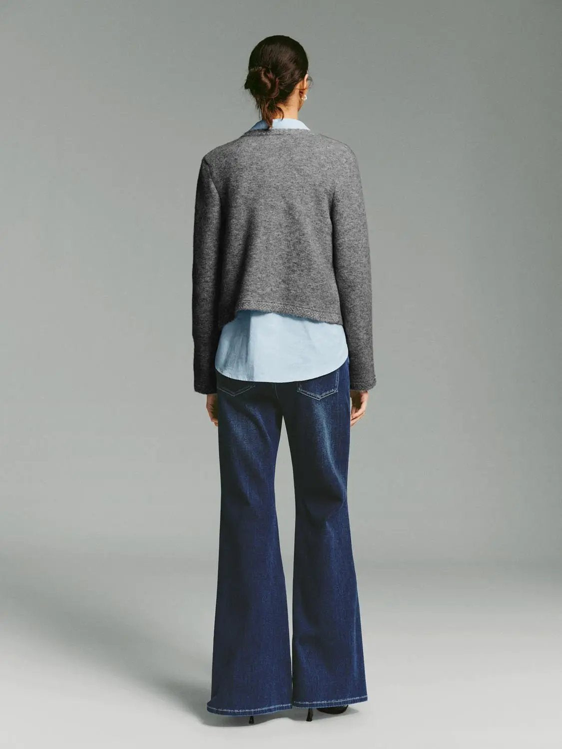 Crew-neck button-front knit cardigan in grey, cropped length, layered over a light blue shirt.