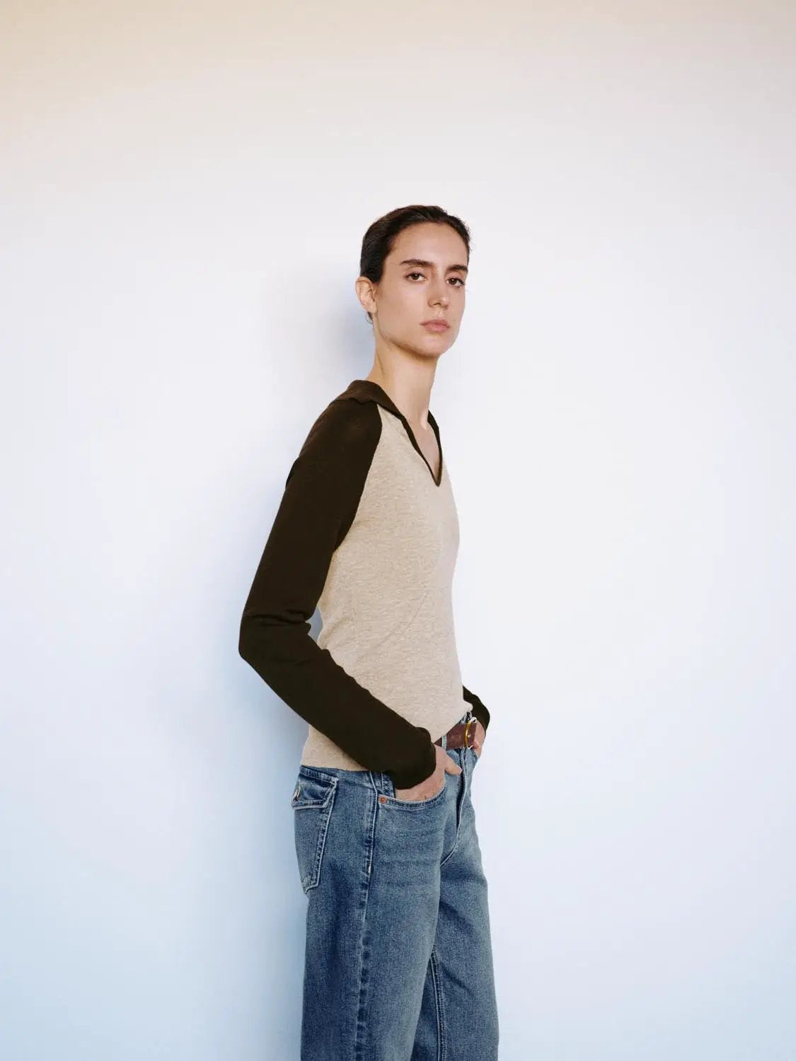 Fitted two-tone V-neck collared long-sleeve knit top with beige body and brown sleeves, paired with blue jeans