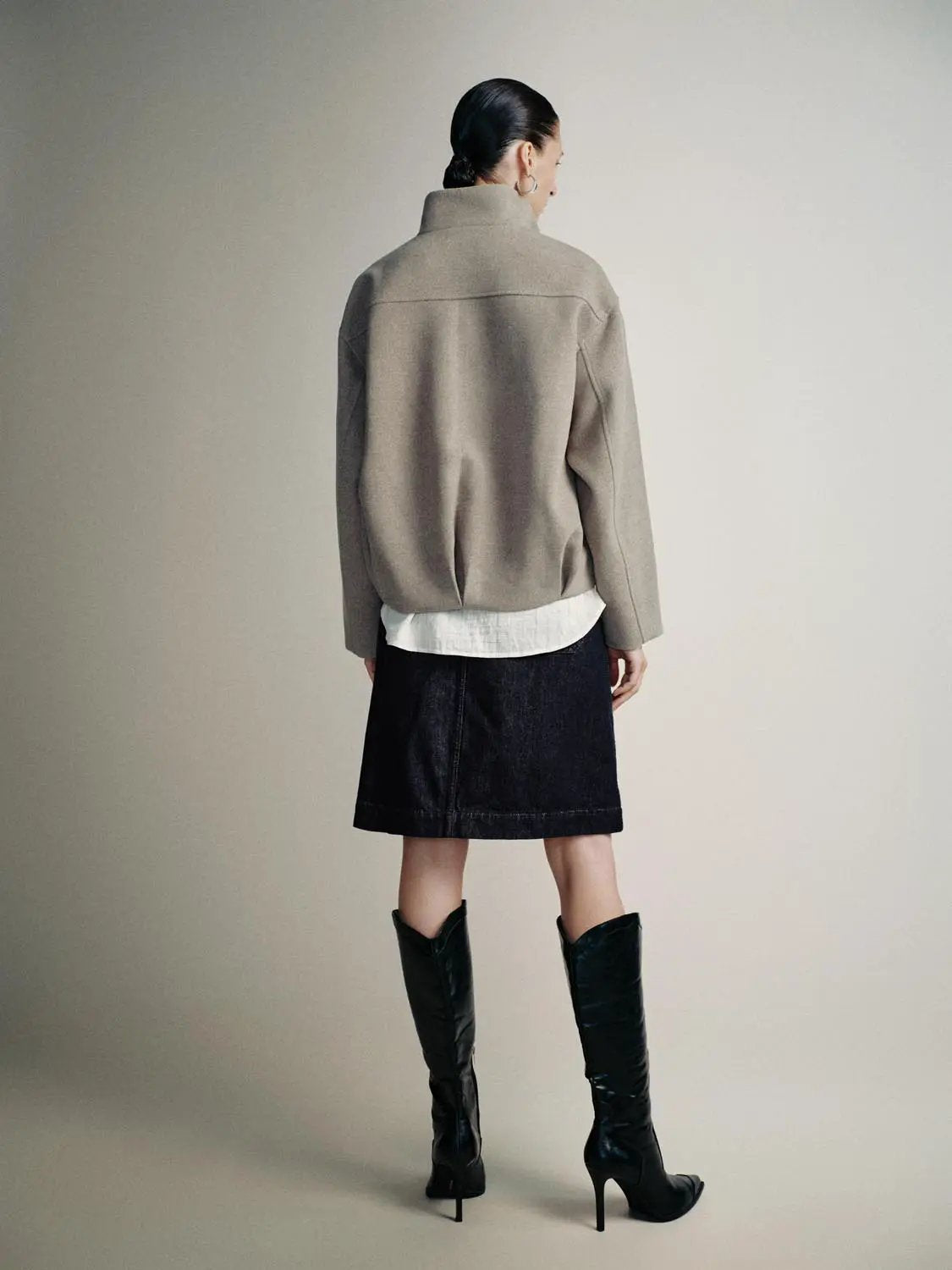 Funnel neck thick jacket in beige, back view; worn with white shirt, black denim skirt, and knee-high boots