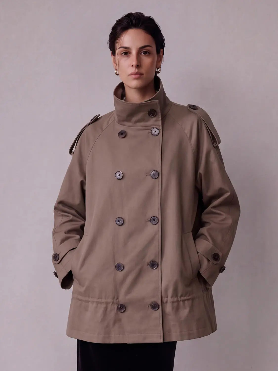 Taupe trench coat, double-breasted with oversized buttons and a high collar.