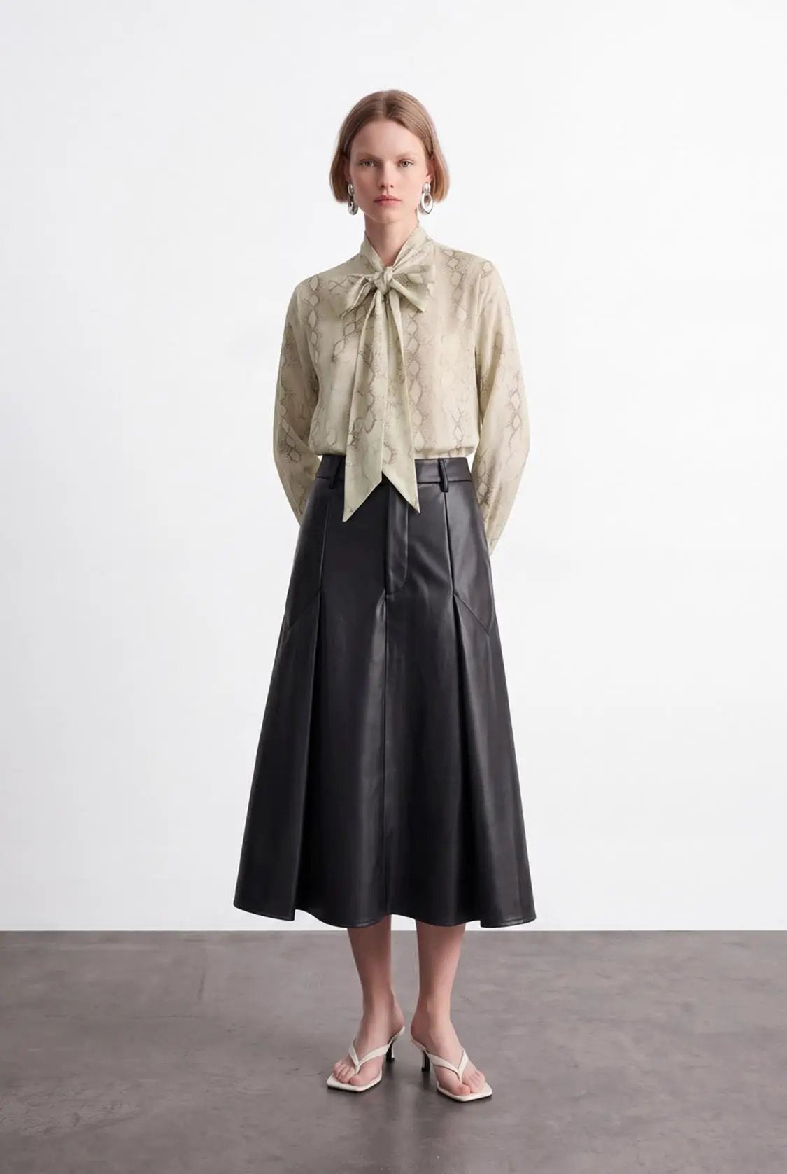 Pleated vegan leather A-line skirt in black; shown with a beige snake-print blouse