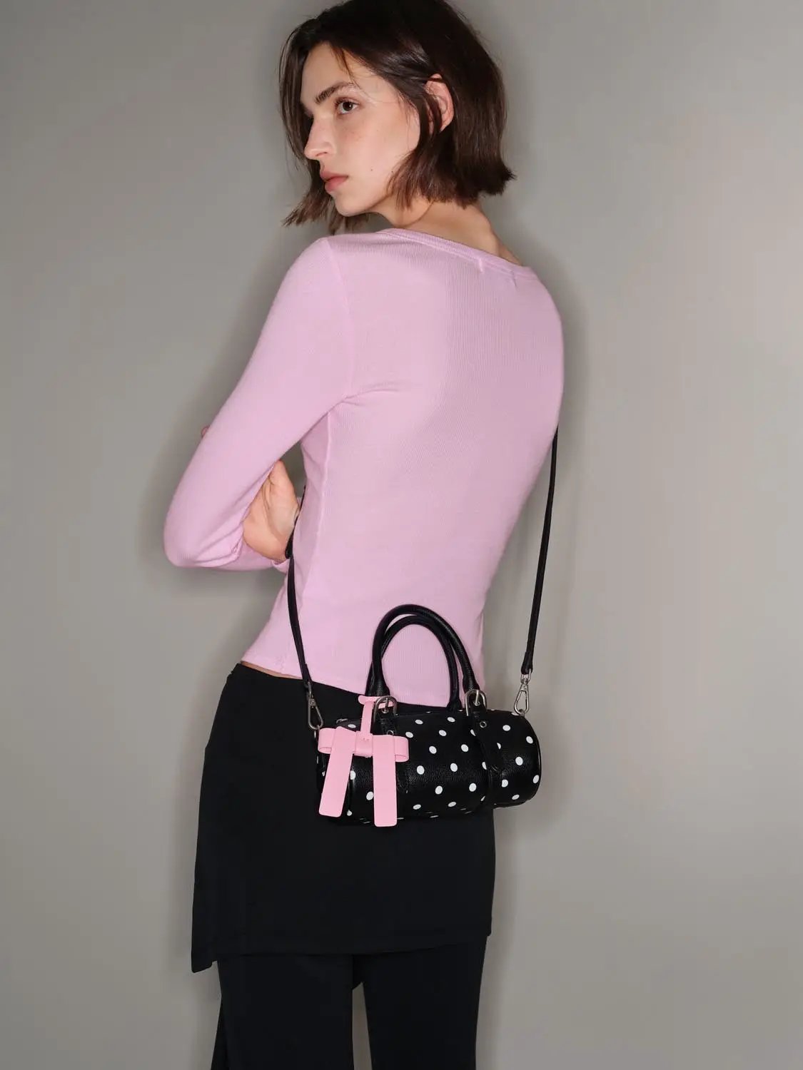 Pink long-sleeve knit T-shirt worn by model with black pants and one polka-dot handbag