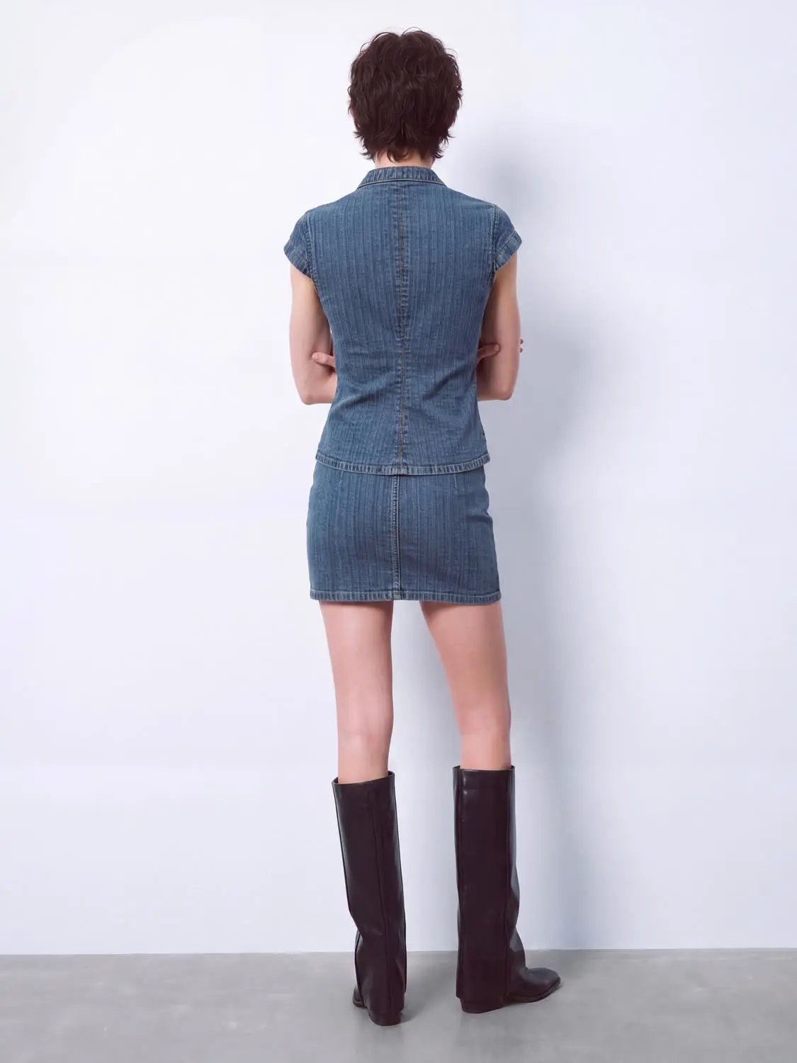 Denim shirt and matching blue denim skirt on model; back view with brown knee-high boots